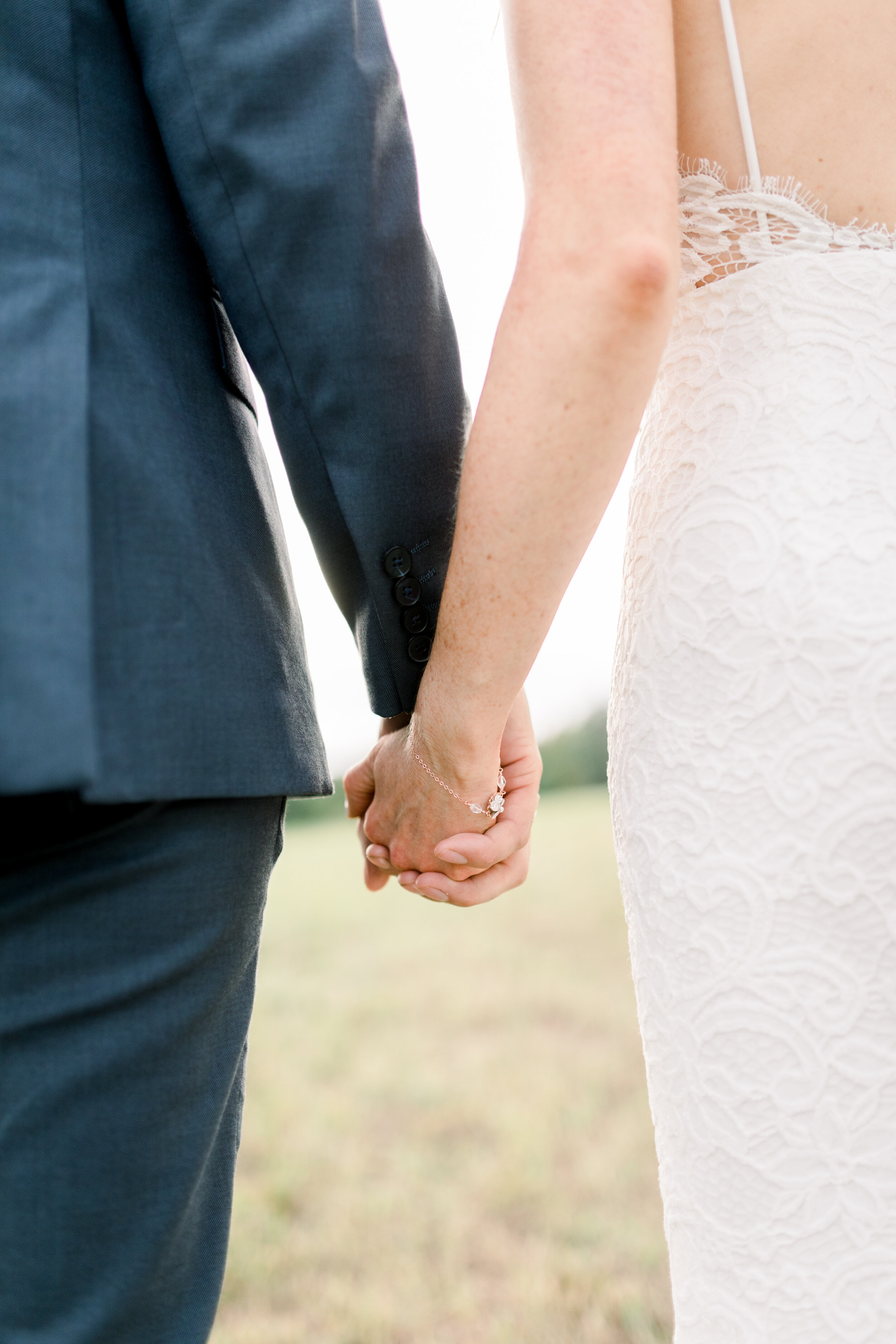  A stunning close-up shot of the wedding dress of a bride on her wedding day in Kinmount, Ontario captured by Chelsea Mason Photography. Beautiful wedding dress details lace wedding dress inspo navy blue wedding attire bride and groom holding hands p