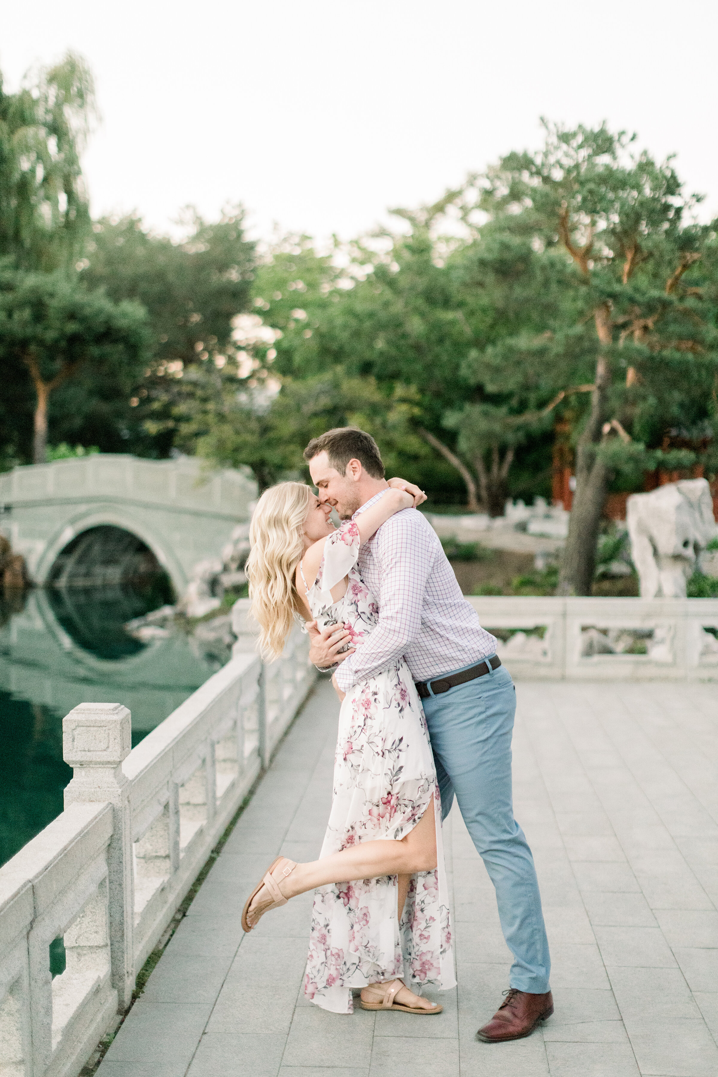  A couple kiss on a beautiful stone bridge in the magical Botanical Gardens in Montreal Canada. Engagement session by Chelsea Mason Photography.  Kissing couple pose inspiration ideas and goals long white flowing floral dress outfit inspiration for w