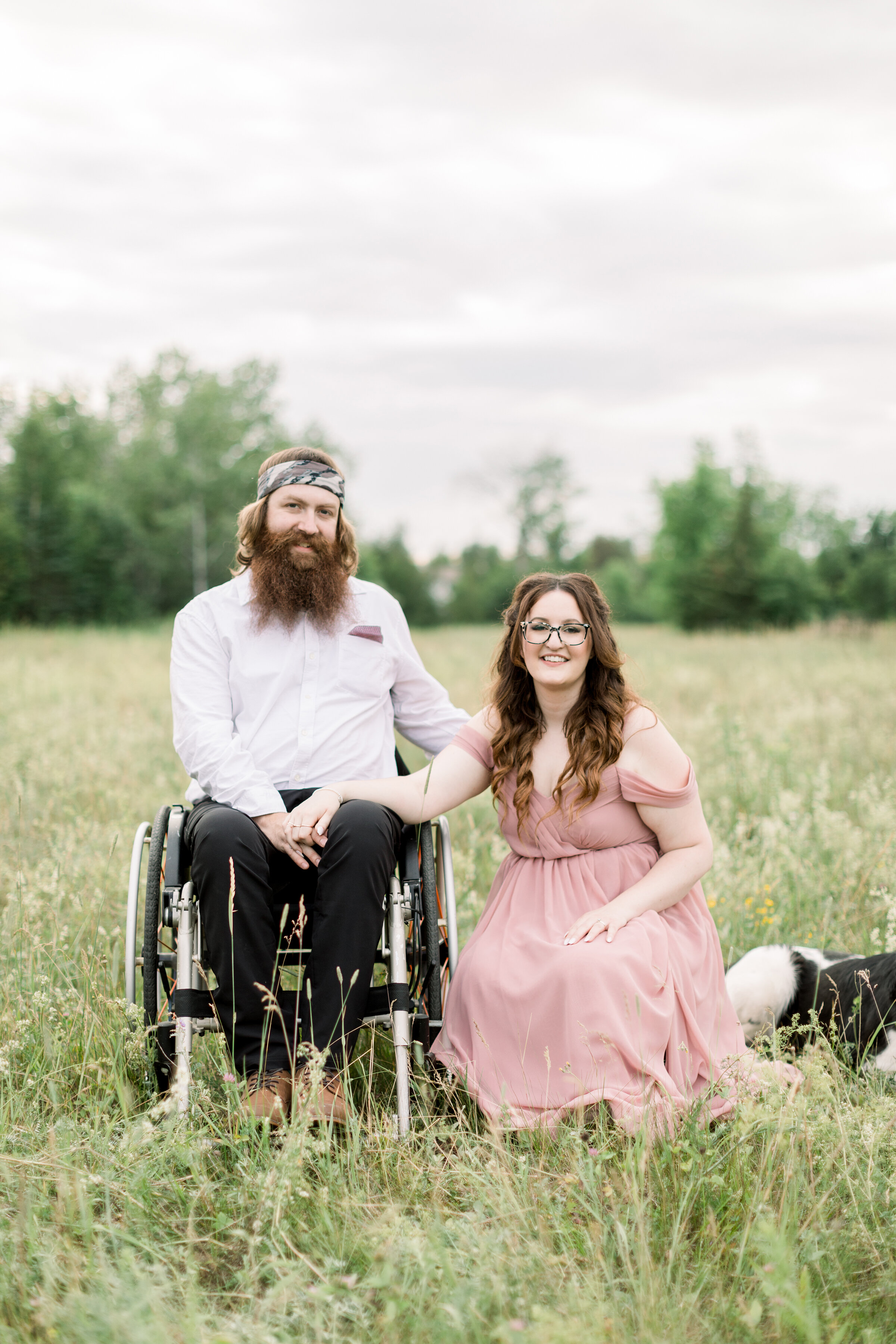  A couple sit together in a beautiful grassy field on a cloudy day in a rustic styled engagement session in Smith Falls, Ontario by Chelsea Mason Photography. Client attire inspiration off the shoulder pink flowy dress inspiration men’s semi formal a