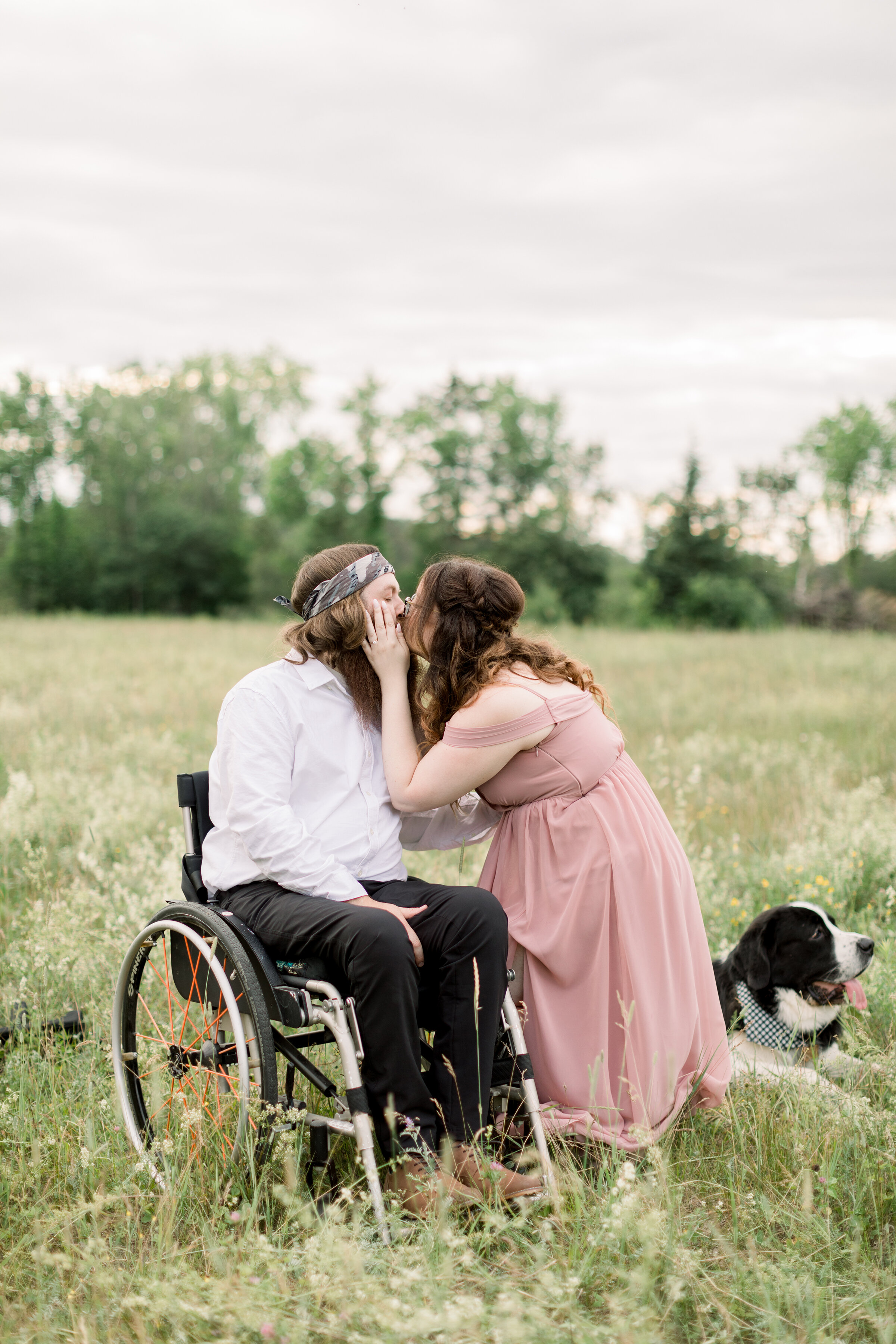  The bride to be kisses her groom in a beautiful paraplegic engagement session in Ontario Canada.  Couple pose with dog inspiration outdoor photo shoot session inspiration ideas and goals client attire inspiration couple pose with one sitting off the
