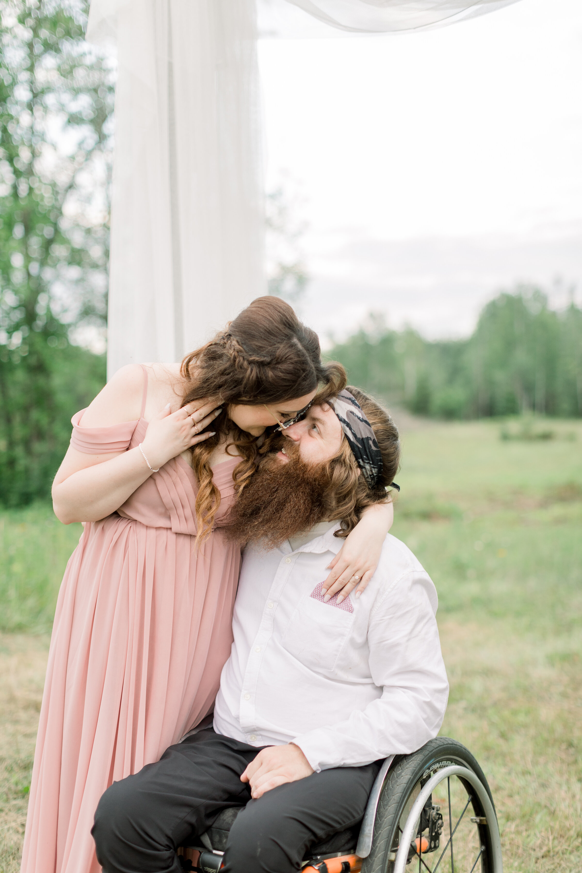  A paraplegic couple go in for a kiss under a elegant rustic arch in a beautiful engagement session by Chelsea Mason Photography in Smith Falls Ontario, Canada. Engagement session pose inspiration ideas and goals couple goals couple pose goals outdoo