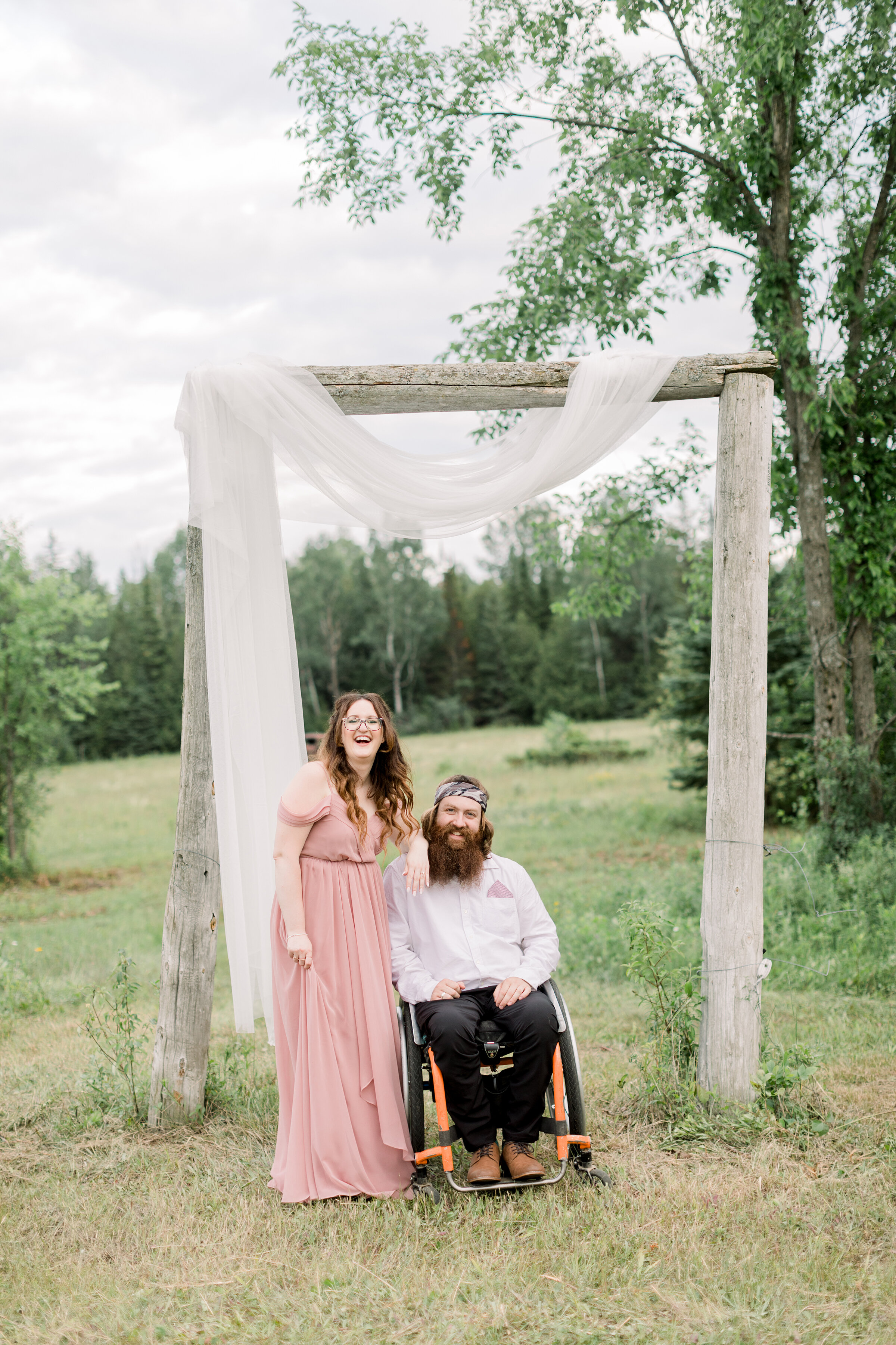  A couple sits and stands together under a beautiful rustic wedding arch in a stunning engagement session for a paraplegic couple. Chelsea Mason Photography couple goals Ontario Canada Smith Falls wedding arch inspiration ideas and goals simple and r