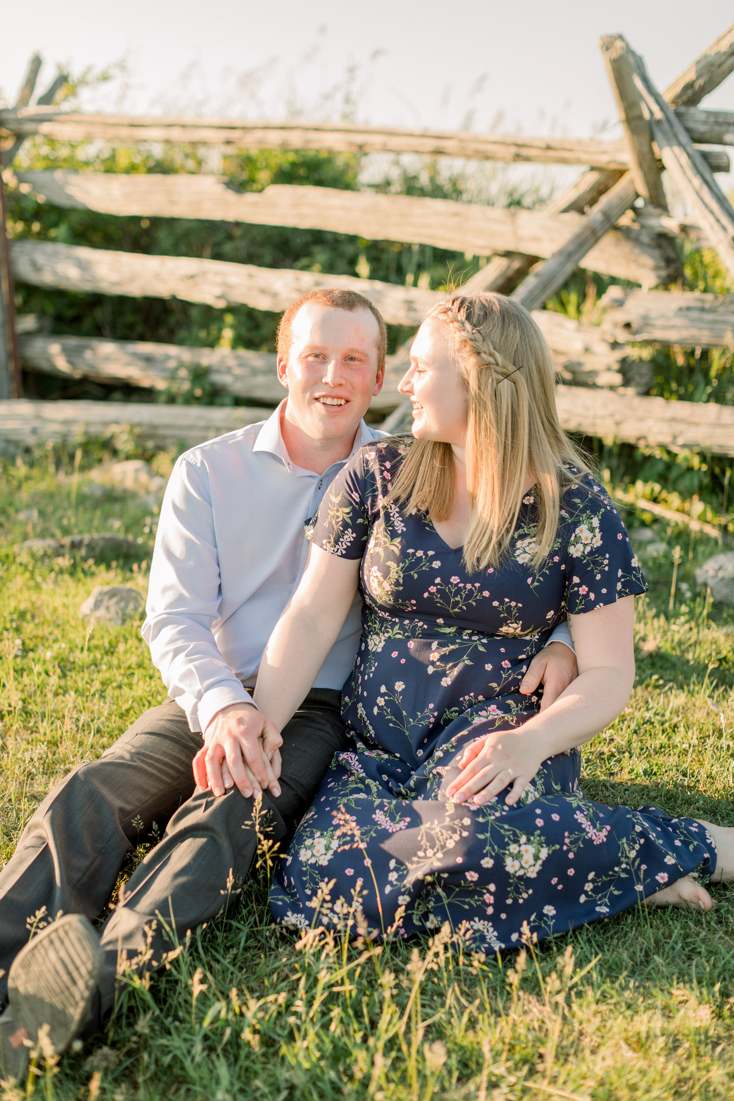  A bride looks at her new fiancé while they sit together on a beautiful farm in Perth, Ottawa. Couple goals couple sitting pose inspiration  wooden fence outdoor country attire engagement outfit inspiration for a country girl semi formal women’s outf