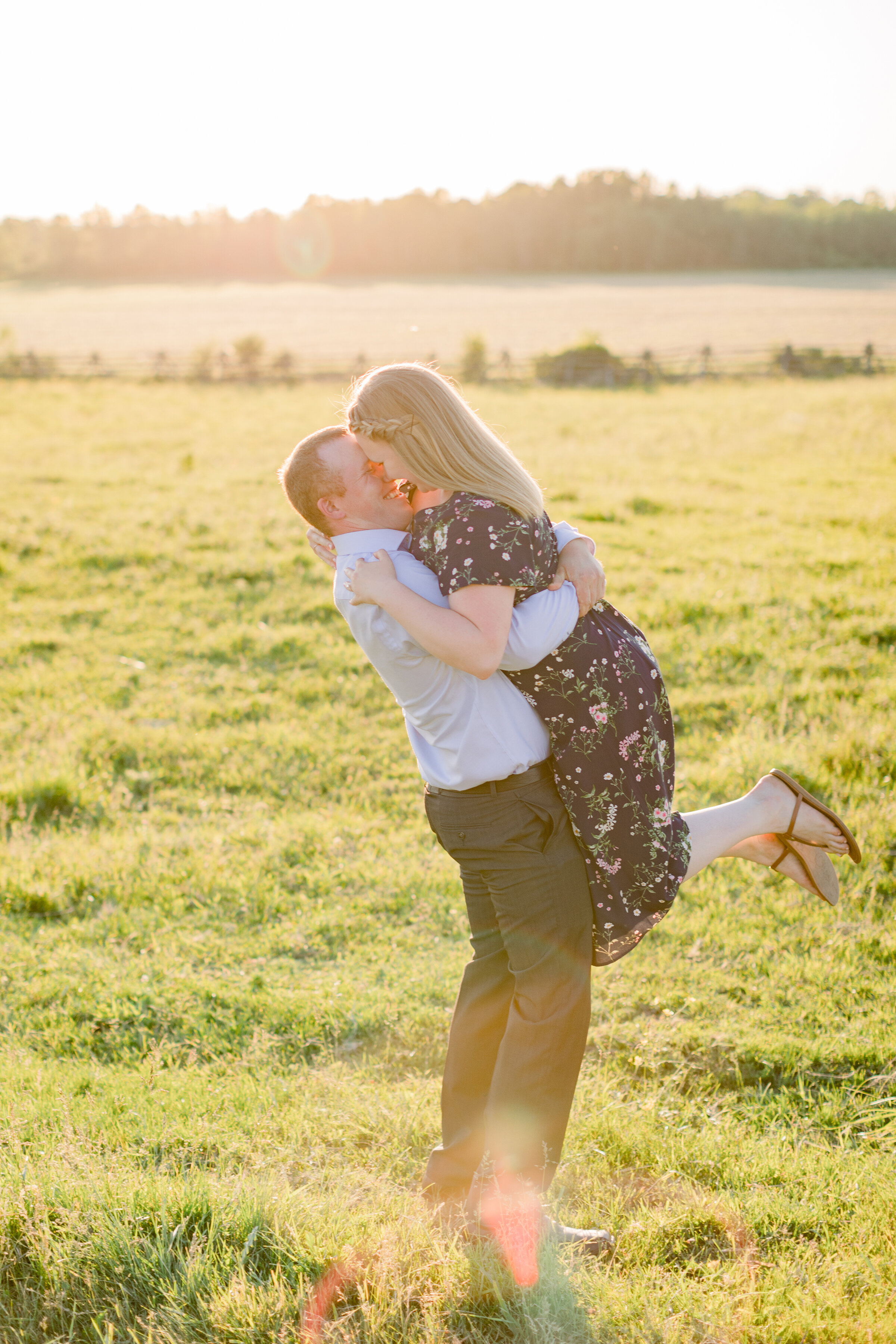  The groom lifts his bride as they kiss in a bright sun filled engagement session by Chelsea Mason Photography. Professional engagement photographer country engagement session country client attire inspiration cowgirl boots outdoor engagement session