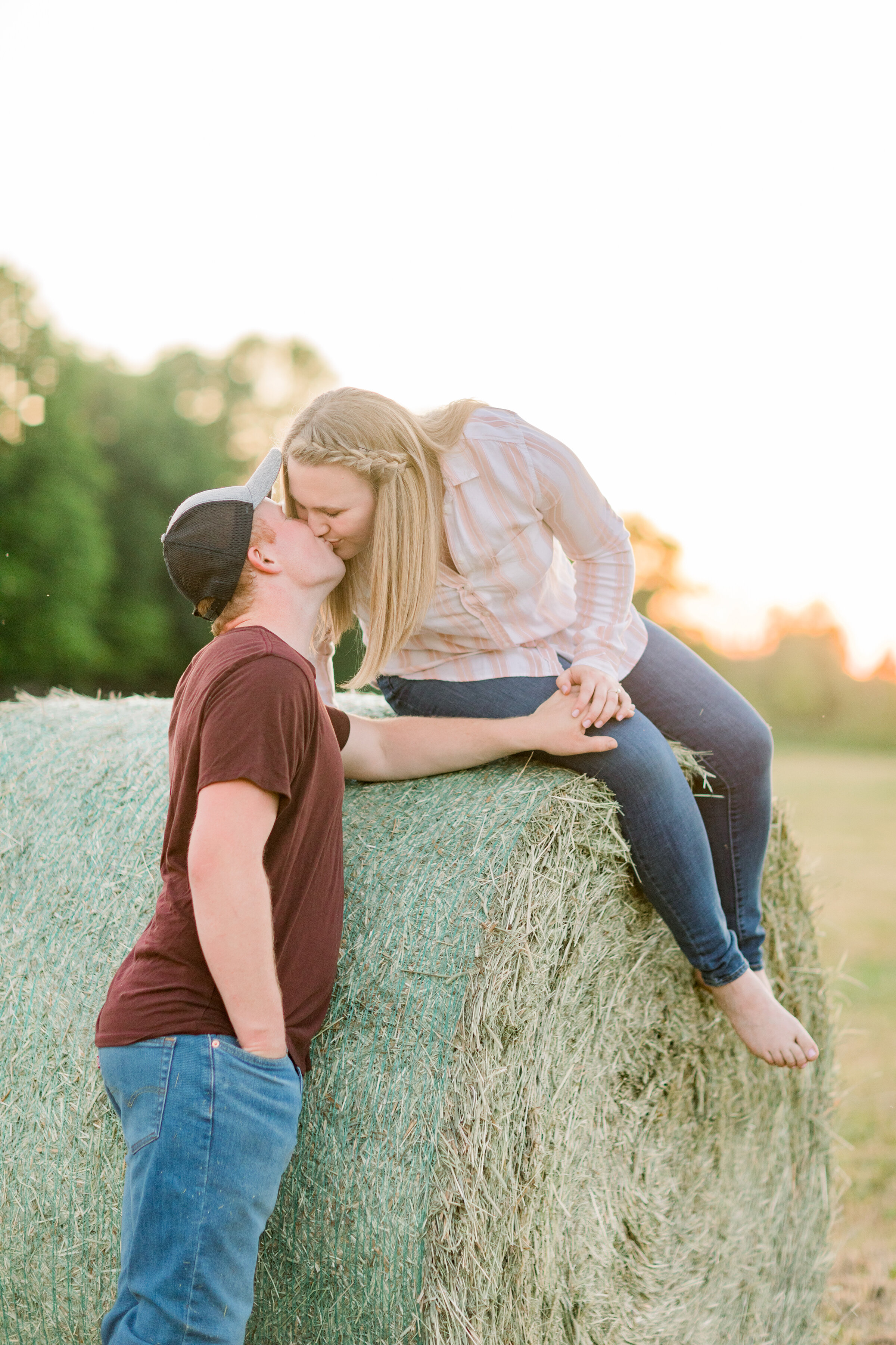  A women leans in for a kiss off a hay bale in a beautiful golden hour engagement session on the farm. Chelsea Mason Photography professional engagement photographer unique country engagement session couple pose inspiration ideas and goals golden hou
