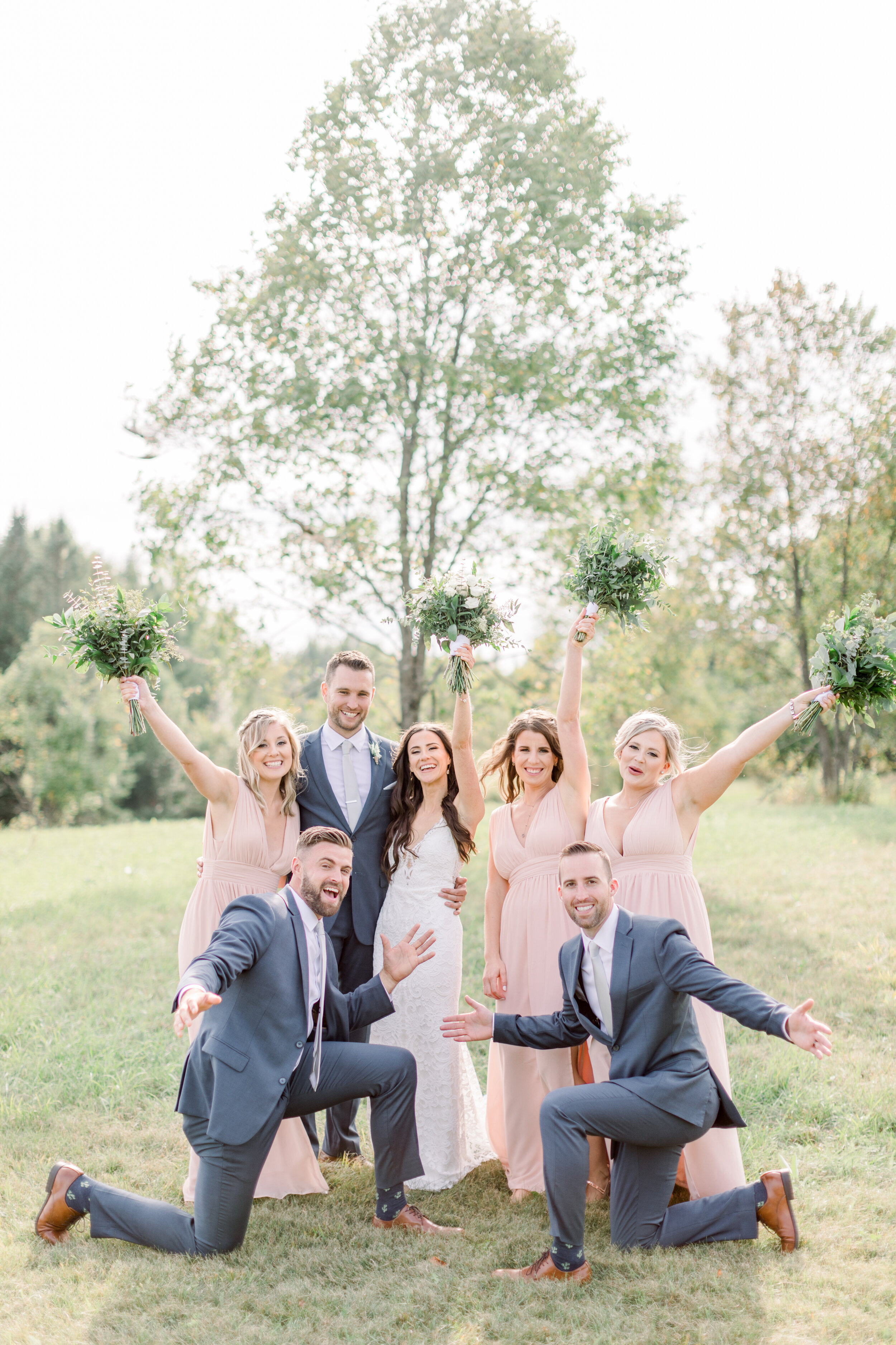  This picture features a fun wedding party celebrating the bride and groom on their big day in Kinmount, Ontario with Chelsea Mason Photography. Wedding party groomsmen bridesmaids light pink dress gray suit wedding attire ontario wedding photographe