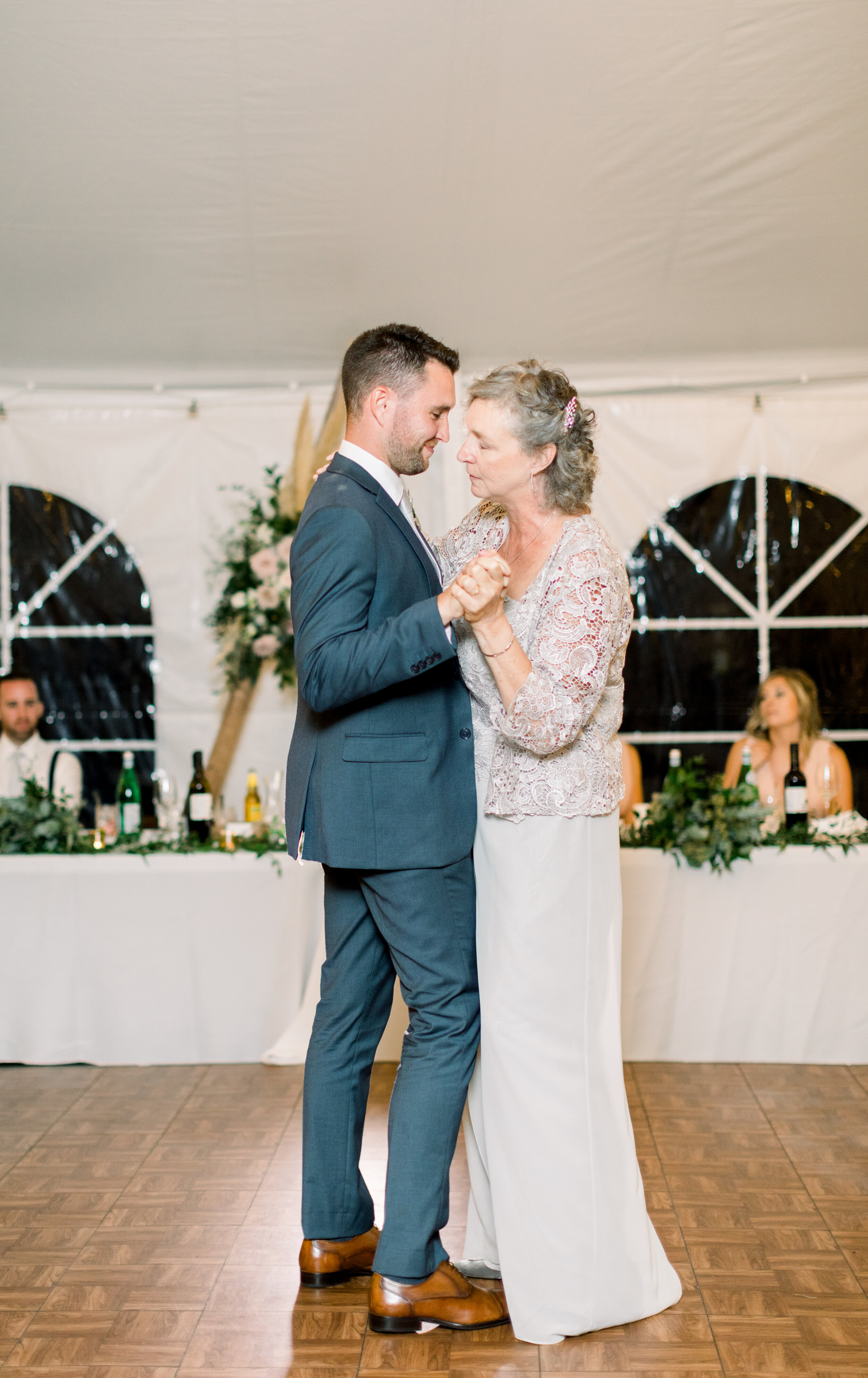  A beautiful moment between the groom and mother of the groom as they dance captured by Chelsea Mason Photography in Kinmount, Ontario. Mother of the groom dance night away dance floor blue navy wedding attire gray dress inspo backyard wedding outdoo