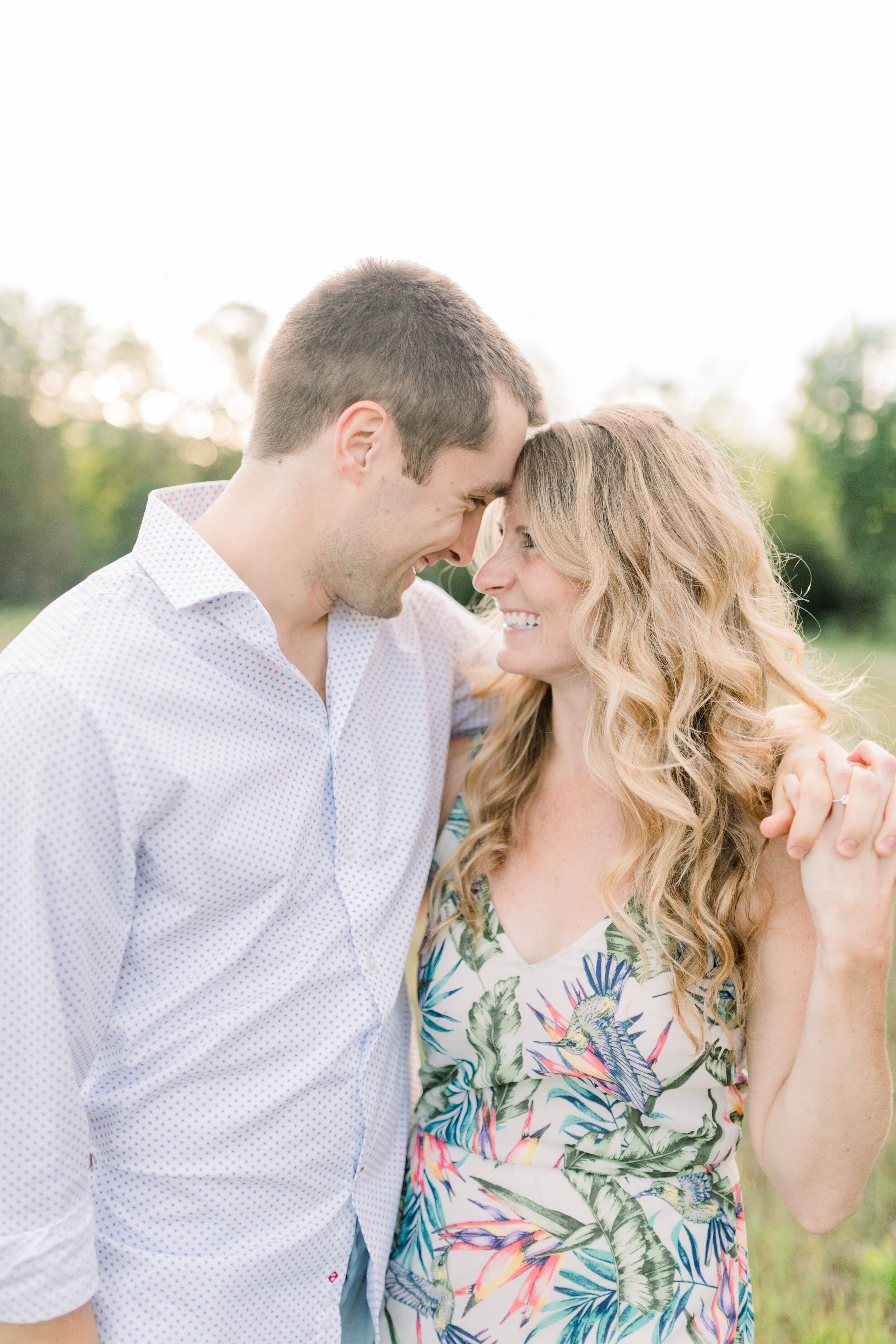  Ottawa, Canada’s Chelsea Mason Photography, captures playful, smiling couple at summer engagement session. muted blue and green engagement session outfit colors, womens v neck tropical print wrap dress, long blonde loose curled womens engagement hai
