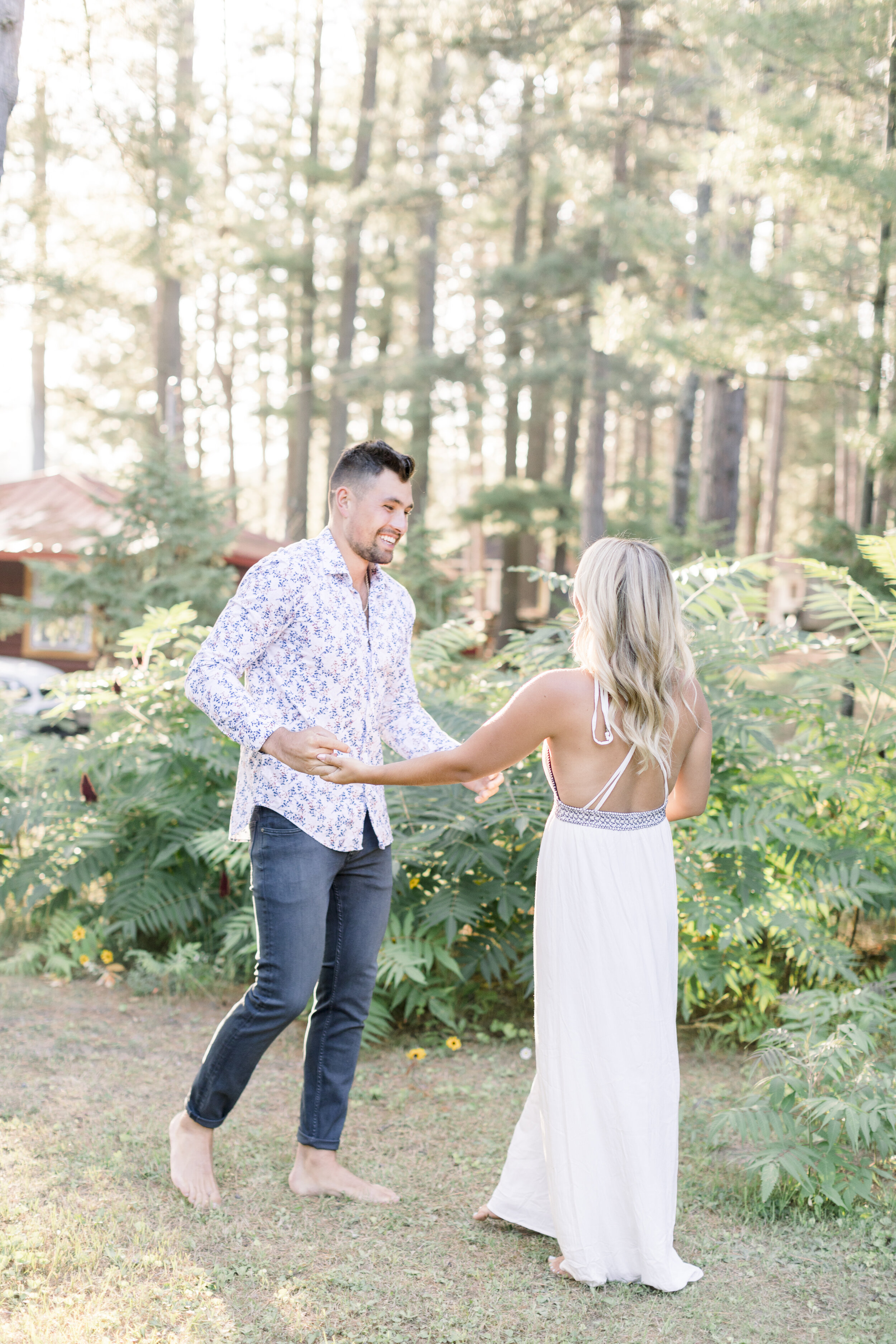  Barefoot couple dancing playfully in the forest for their quebec engagement sessions at sunset at a lakeside cottage. Quebec engagement session locations dancing poses for engagement posing inspo for engagement photography best quebec photographer f