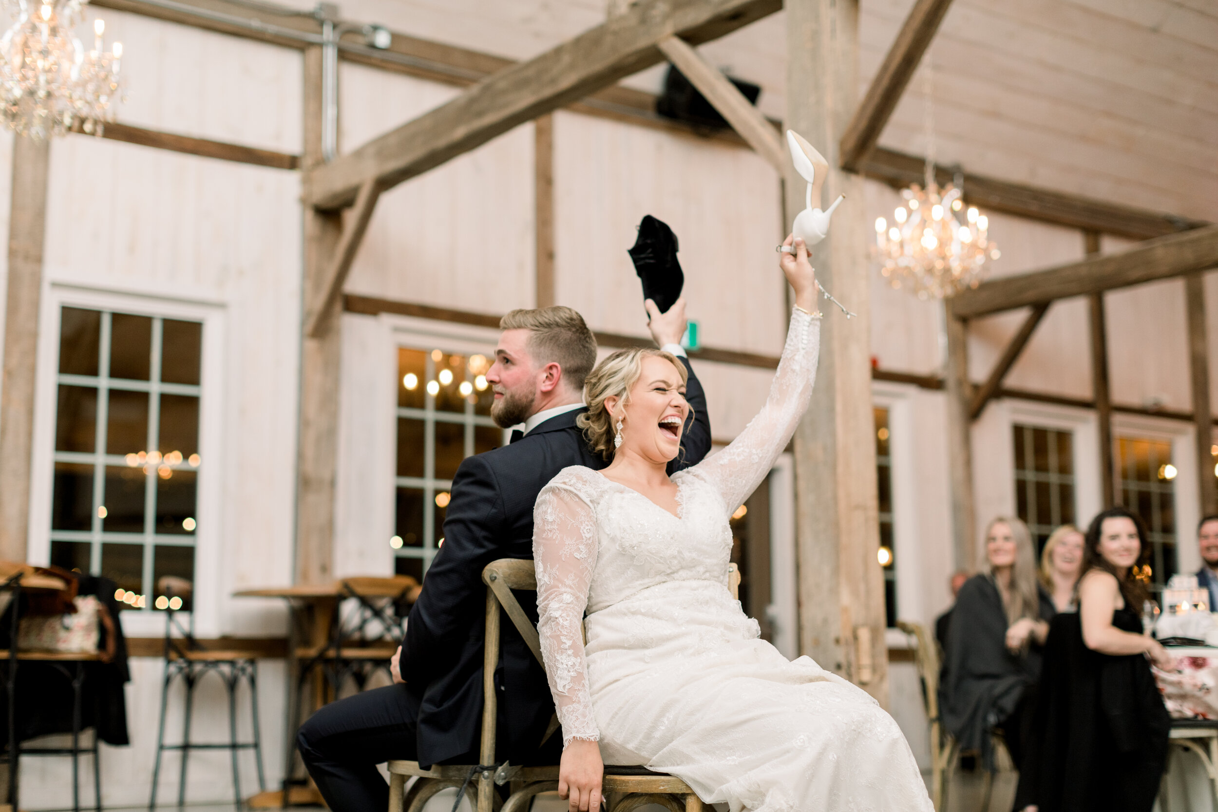  Ottowa bride and groom at their wedding reception at the rustic stonefield wedding venue in ottowa lifting their shoes and laughing as the play the ‘shoe game’ in front of their guests. Wedding games bridal heels unique wedding dress wedding recepti