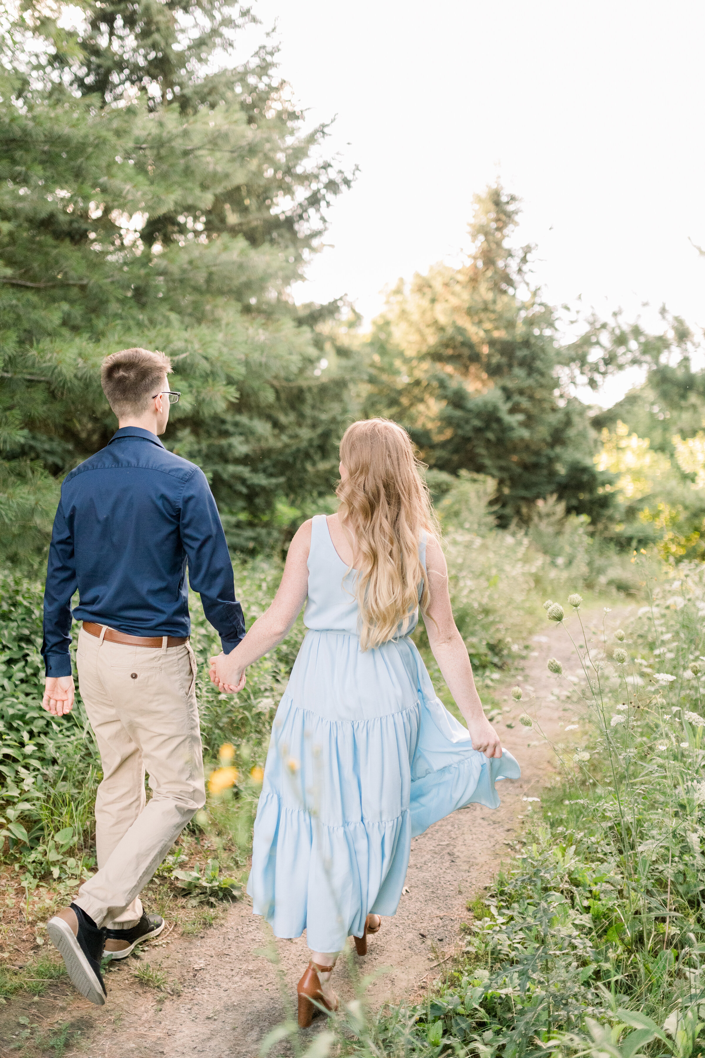  A couple walk together down a wild flower lined path in Dominion Arboretum, Ottawa in an engagement styled photo shoot by Chelsea Mason Photography. Professional engagement photographer outdoor photo shoot location inspiration ideas and goals walkin