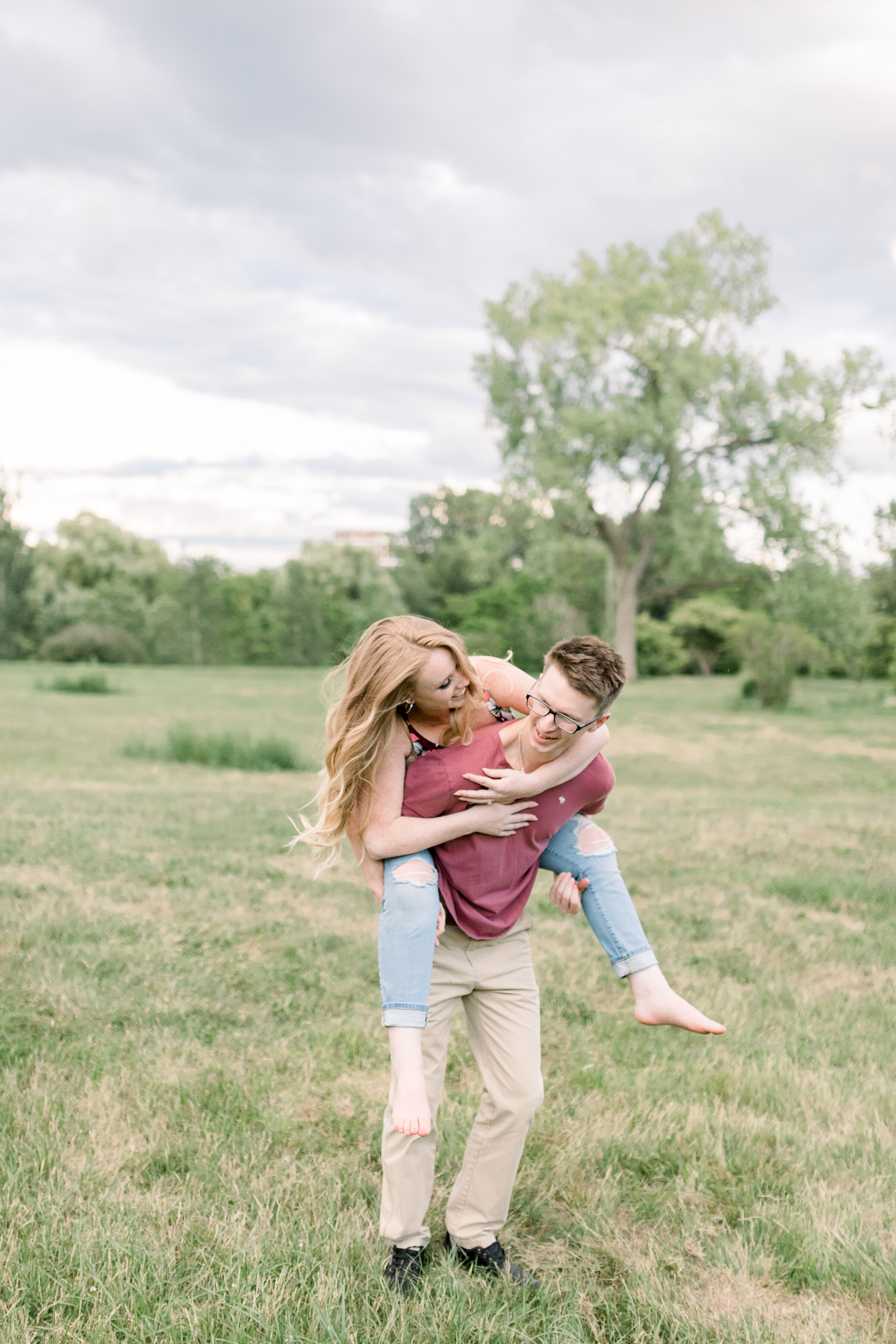  A happy man gives his laughing fiancé a piggy back ride in a playful engagement session at the Dominion Arboretum in Ottawa by Chelsea Mason Photography. Professional Ottawa photographer engagement photographer playful couple pose inspiration ideas 