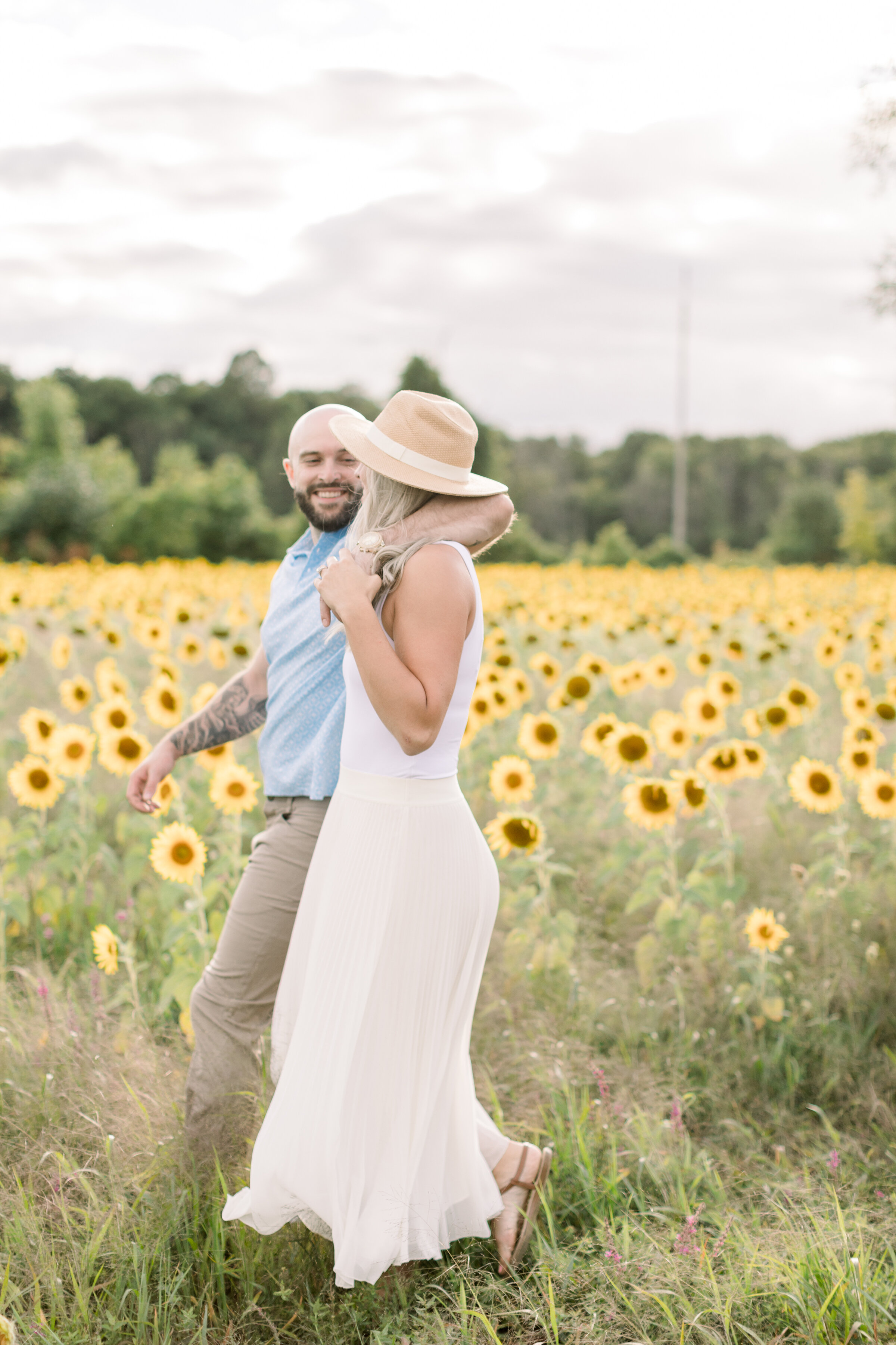  A handsome groom wraps his arm around the shoulders of his fiancé in a sunflower themed engagement session in the bright and airy Ottawa, Ontario. Professional engagement photographer Chelsea Mason Photography couple goals couple pose inspiration id