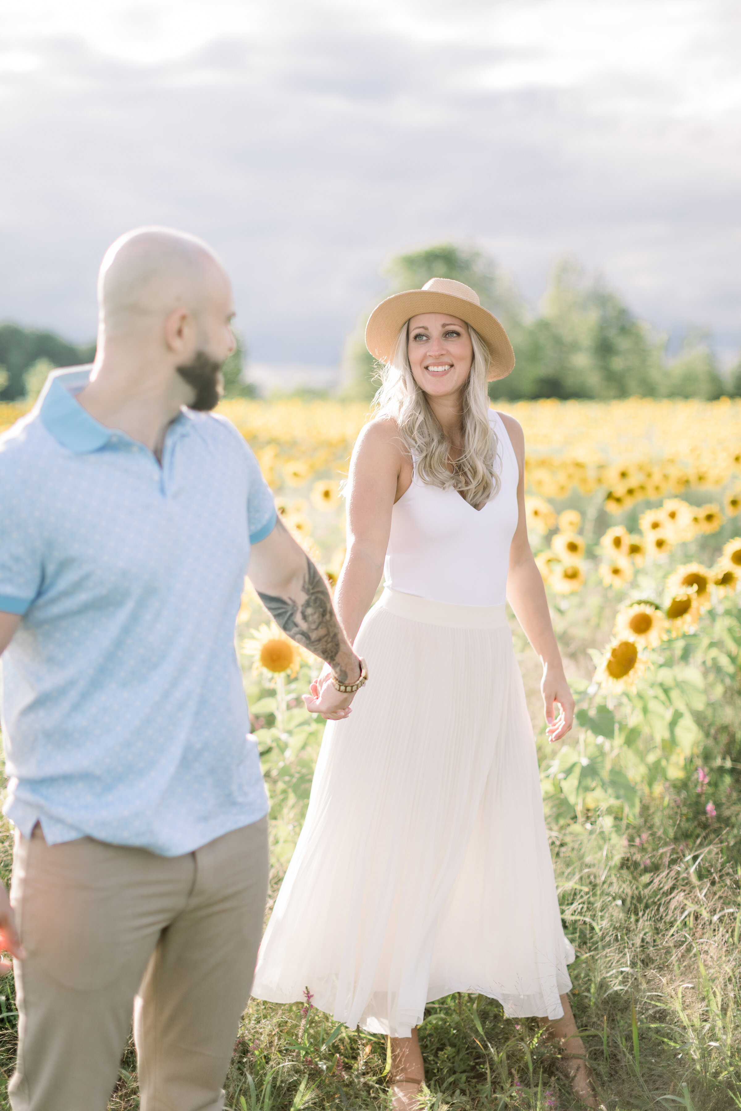  A beautiful women smiles lovingly at her soon to be husband in a beautiful unique engagement session in the sunflower fields of Ashton, Ontario. Chelsea Mason photography professional Ontario engagement photographer summer engagement session couple 