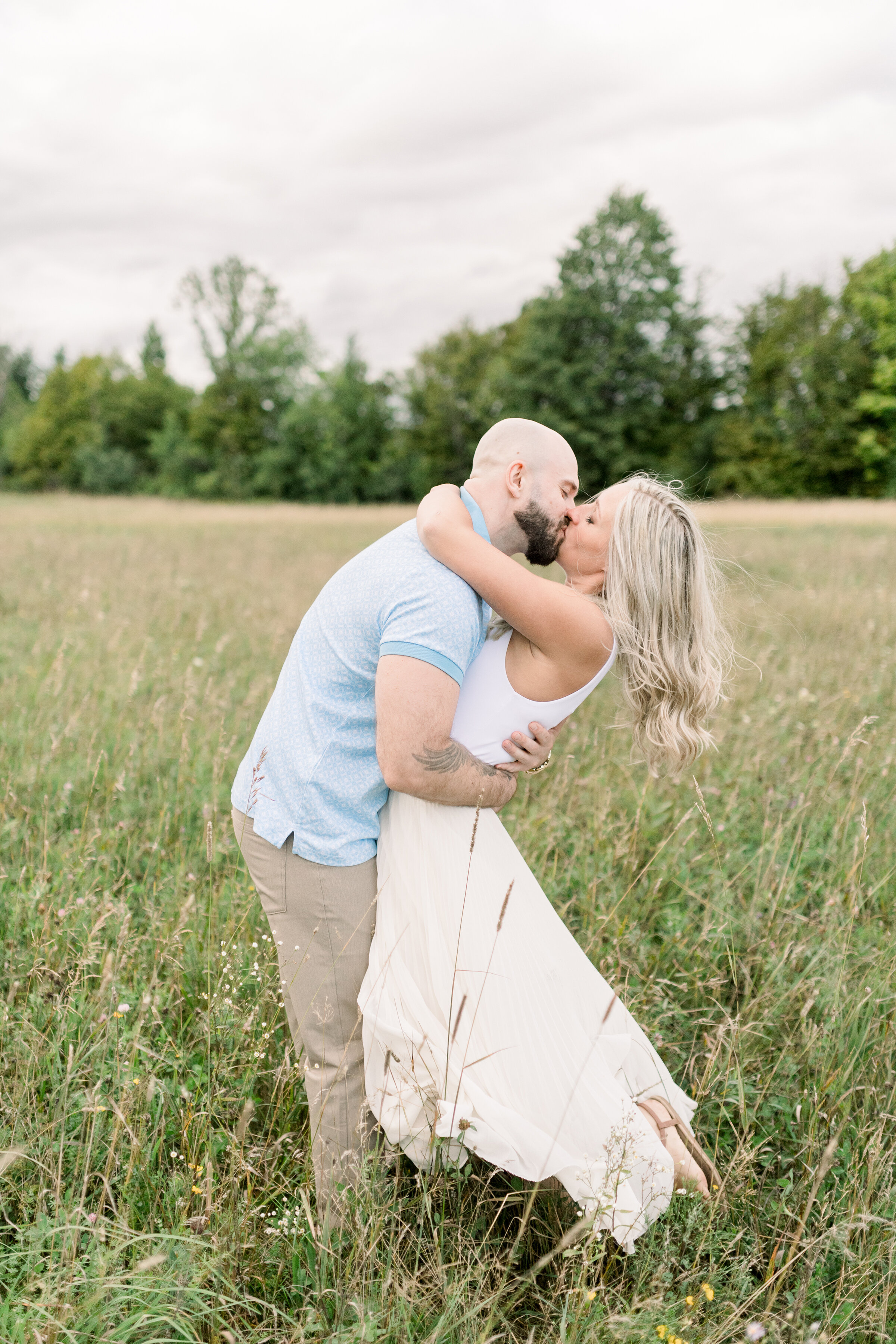  A handsome groom dips his beautiful fiancé as they kiss in a stunning grassy field in an engagement session by Chelsea Mason Photography in Ashton, Ontario. Couple goals couple kissing pose inspiration ideas and goals outdoor photo shoot inspiration