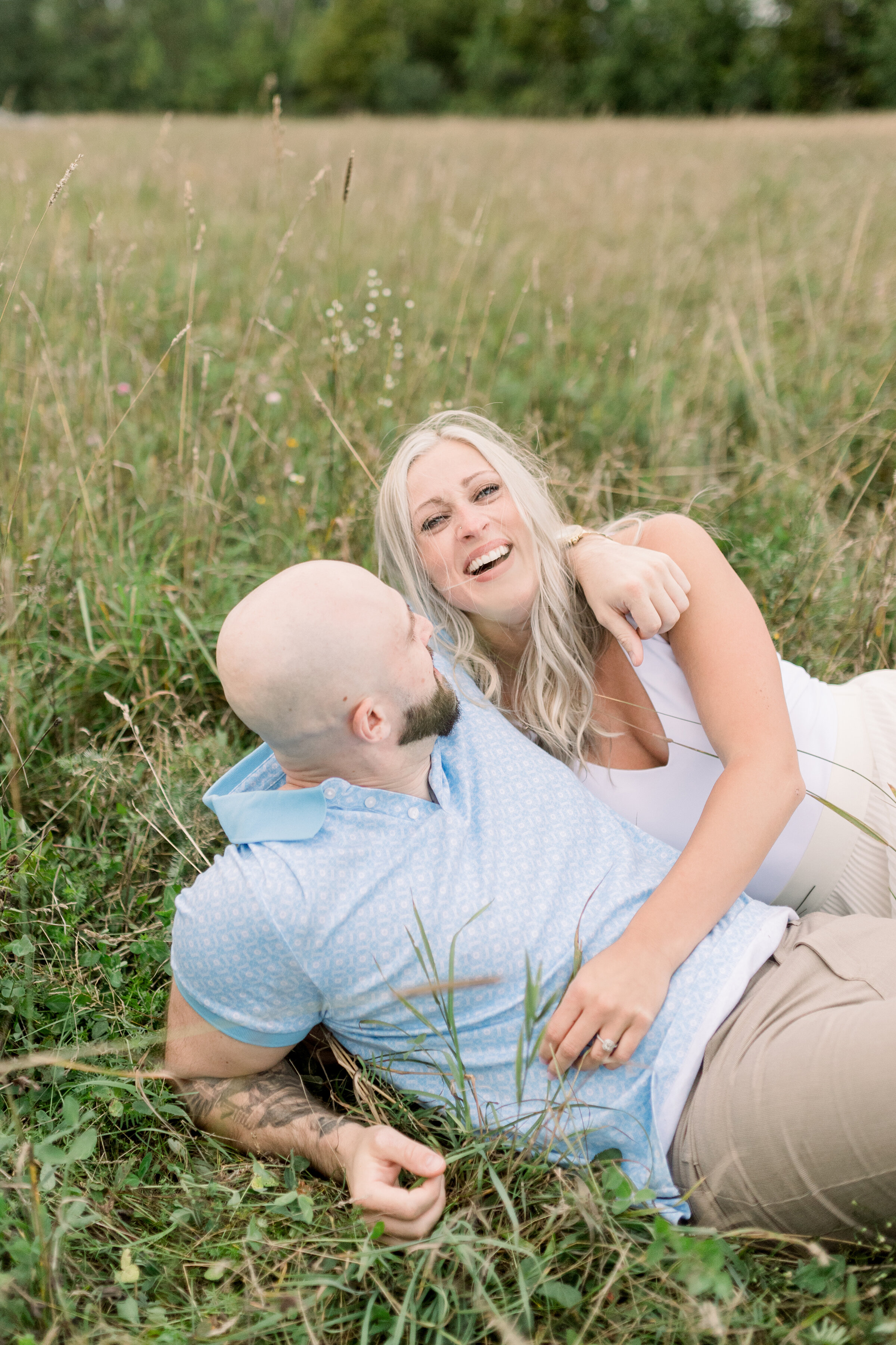  A glowing couple laugh together as they lay in the grass in Ashton, Ontario in an fun engagement session by professional Ontario photographer Chelsea Mason Photography. Couple laying down pose inspiration coupe goals summer engagement session attire