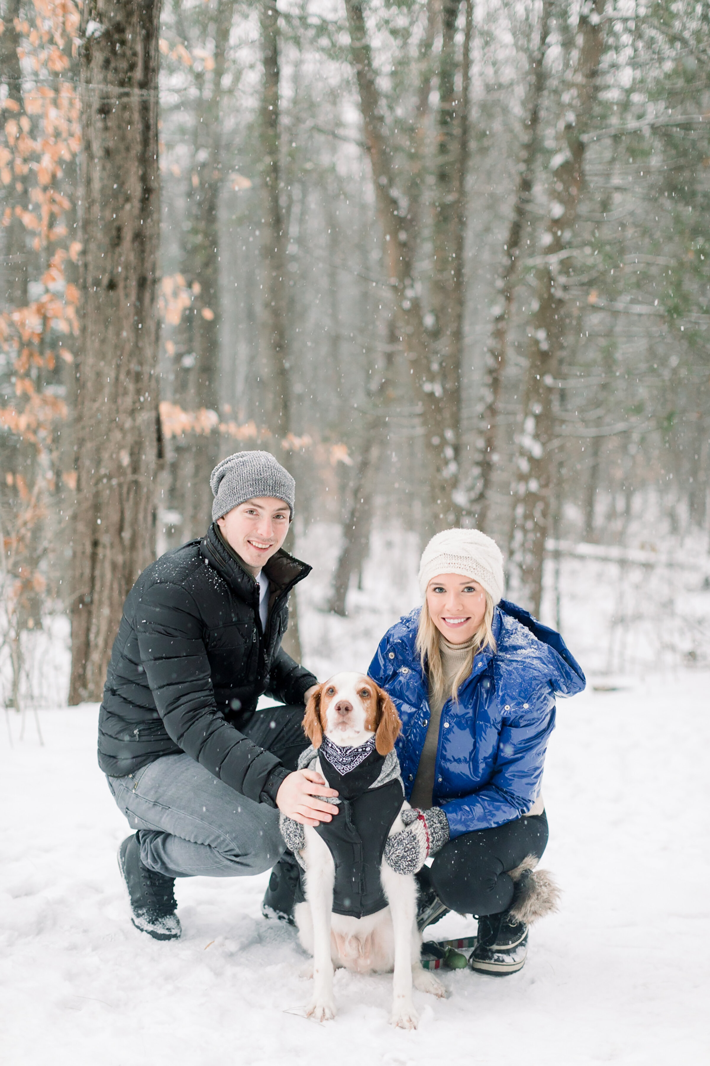  A happy couple squat in the Pinhey’s Trails trees next to their adorable dog in a winter maternity session by professional Ottawa photographer Chelsea Mason Photography. Winter family photo shoot inspiration ideas and goals couple goals small family