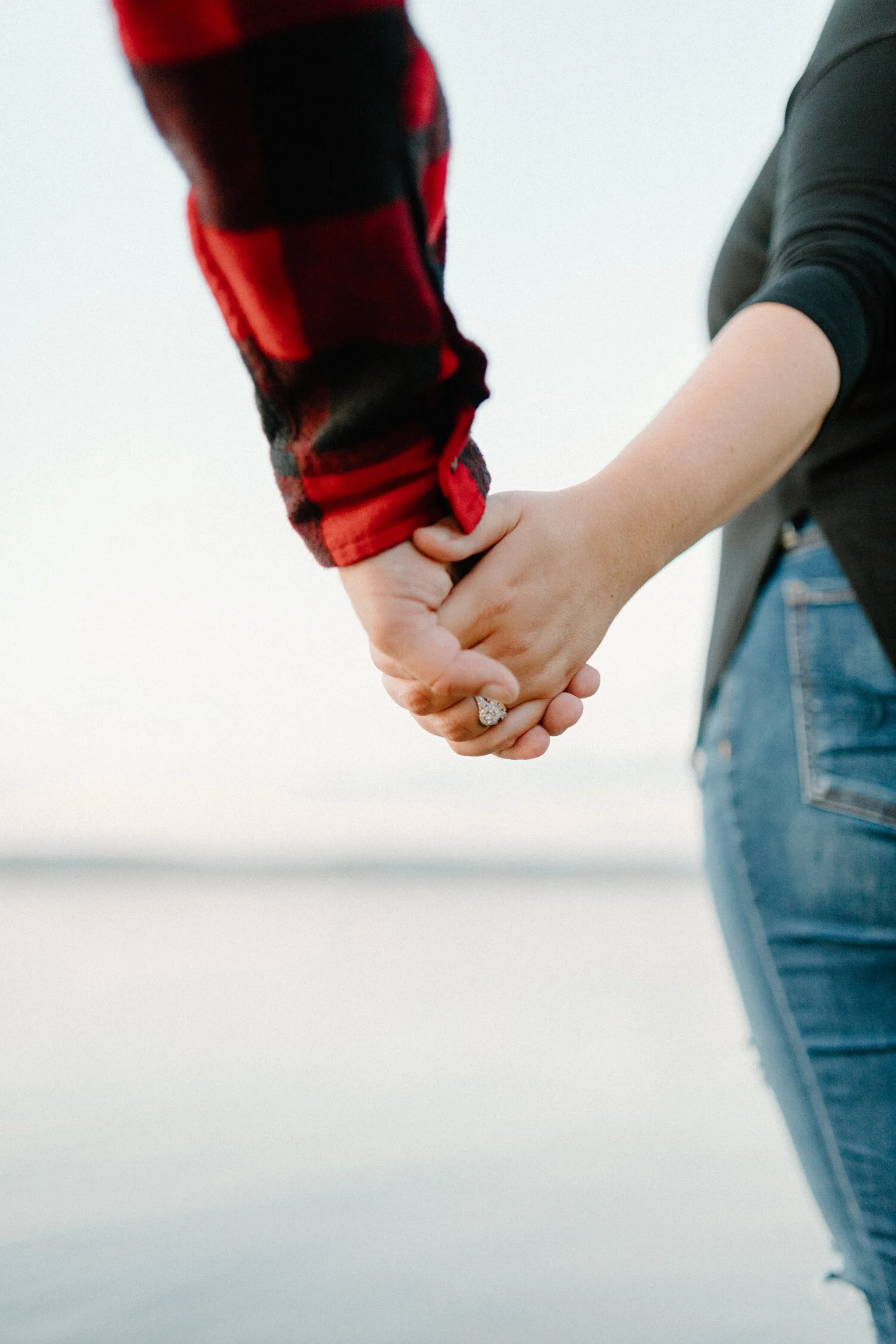 Ottawa, Canada’s Chelsea Mason Photography captures up-close details of this couple holding hands along a beach and features this bride-to-be’s engagement ring. White gold diamond halo engagement ring, couple holding hands on the beach, ottawa canad