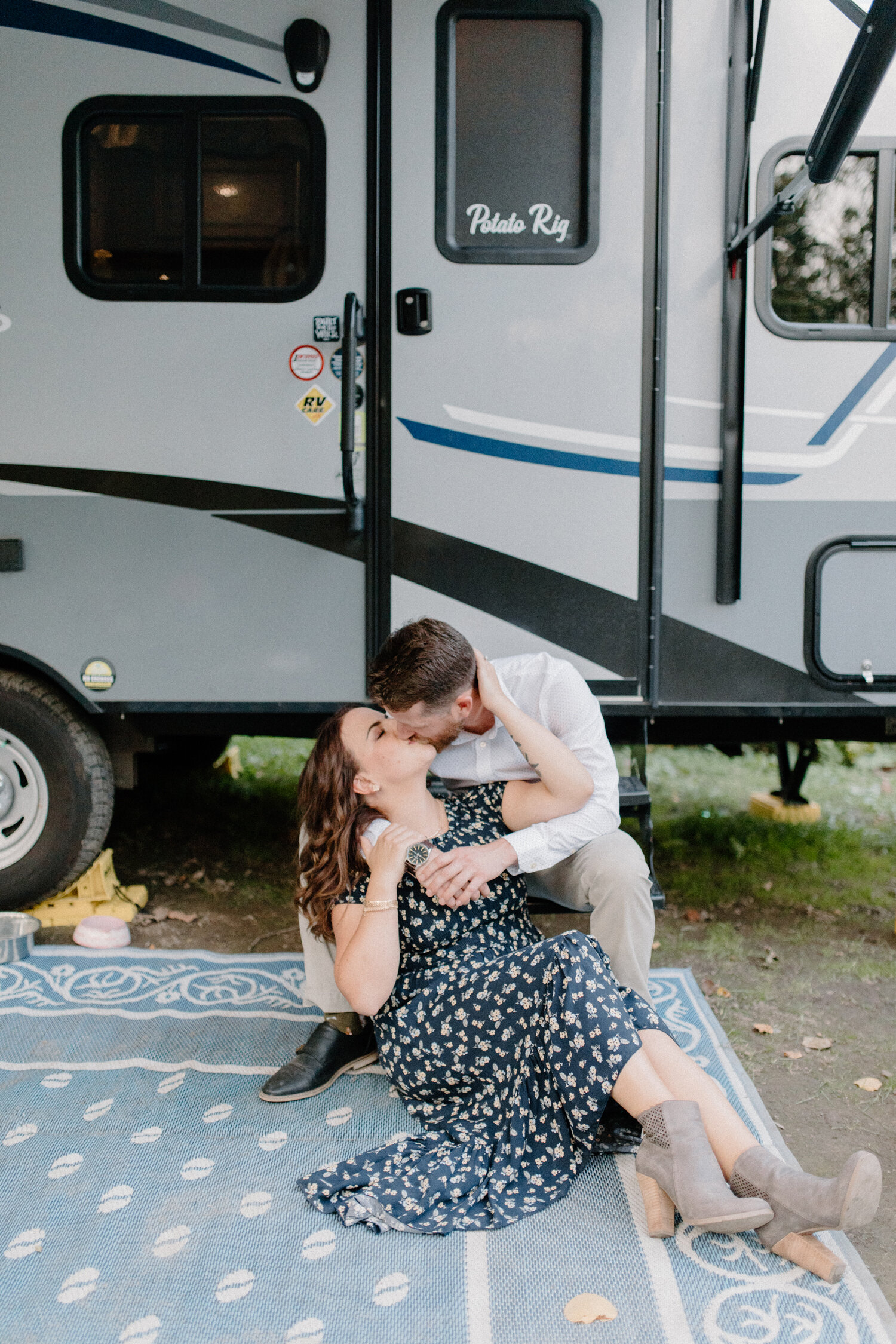  Sitting on a picnic blanket in front of their camper, Ottawa, Canada’s Chelsea Mason Photography captures this couple smiling and cuddling during their engagement session. Camping engagement session, outdoorsy camping engagement session, picnic blan