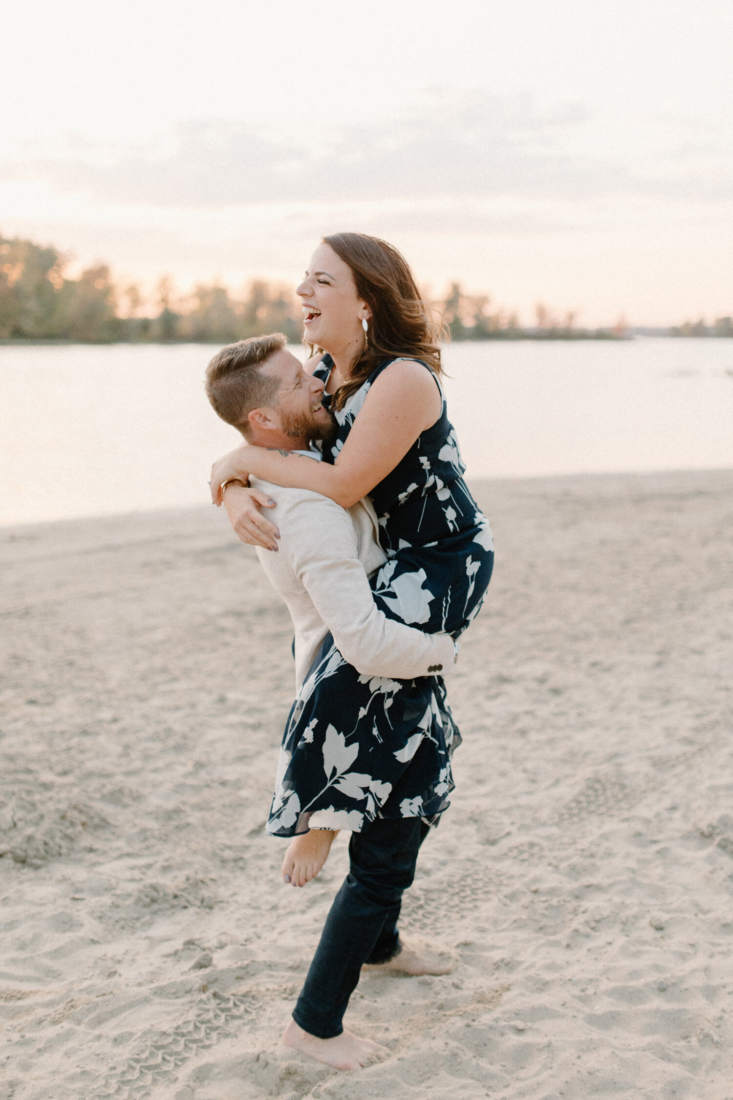  Chelsea Mason Photography captures this woman laughing while her fiance picks her up and runs along the beach shore in Ottawa, Canada. Beach ottawa canada engagement session, photographer ontario canada, formal beach outfits, laughing playful engage