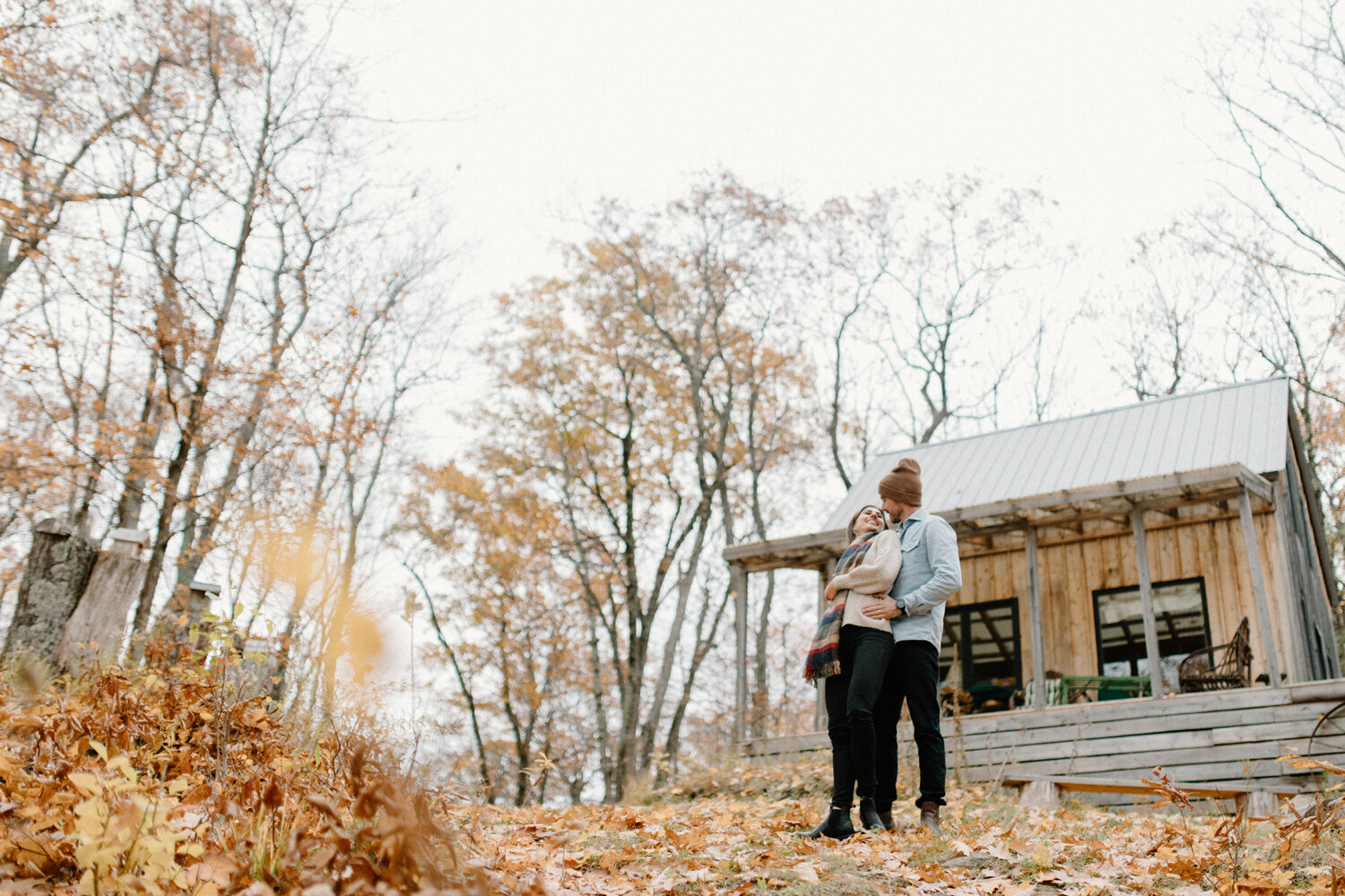  During their photoshoot with Quebec, Canada engagement photographer, Chelsea Mason Photography, this couple embraces one another in front of their wooded cottage. Wooded cottage overcast engagement session, autumn engagement photographer quebec cana