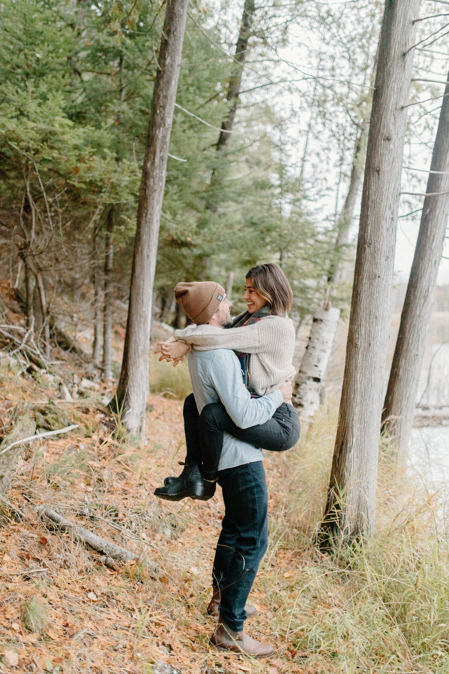  On the shore of this Quebec, Canada lake, Chelsea Mason Photogrpahy captures this woman wrapping her arms and legs around her fiance during their autumn engagement session. Autumn in quebec canada family photos, woman wrapping legs and arms around h