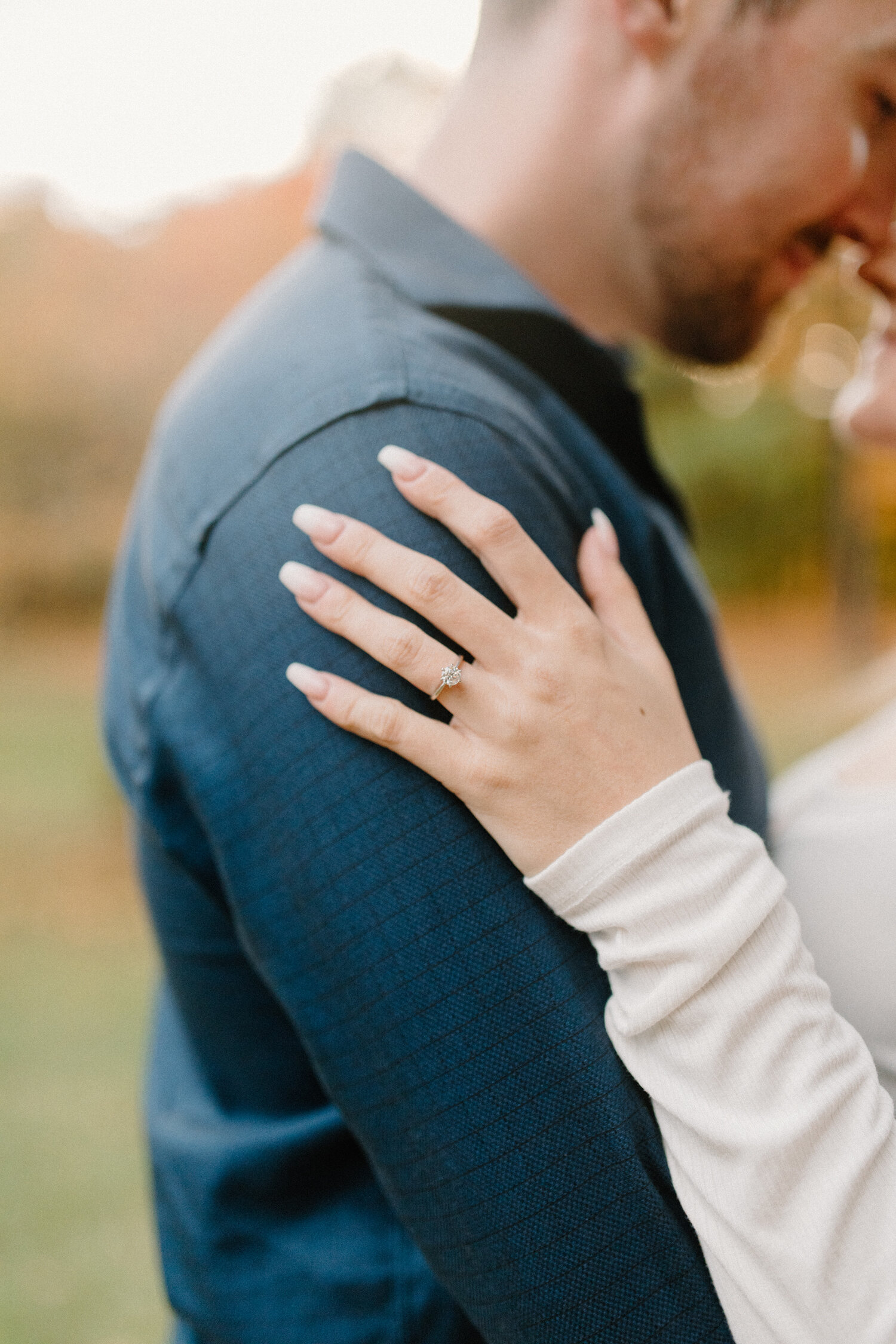 During this Quebec, Canada engagement session, Chelsea Mason Photography captures an up-close ring shot of this white gold solitaire diamond ring. round solitaire diamond white gold ring, mens checkered dark blue button up shirt, womans hand on groo