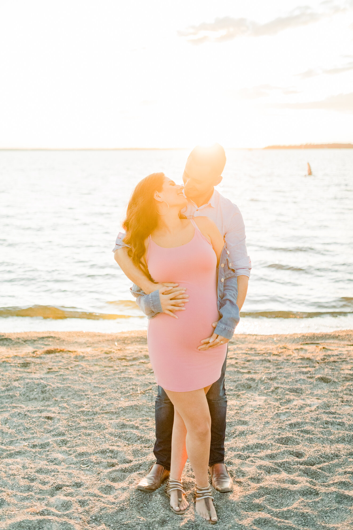  Ontario, Canada maternity photographer, Chelsea Mason Photography captures this expectant couple sharing a romantic moment of embrace along the Brittania Beach shoreline during their session. fitted pink maternity dress, oversized off the shoulder d
