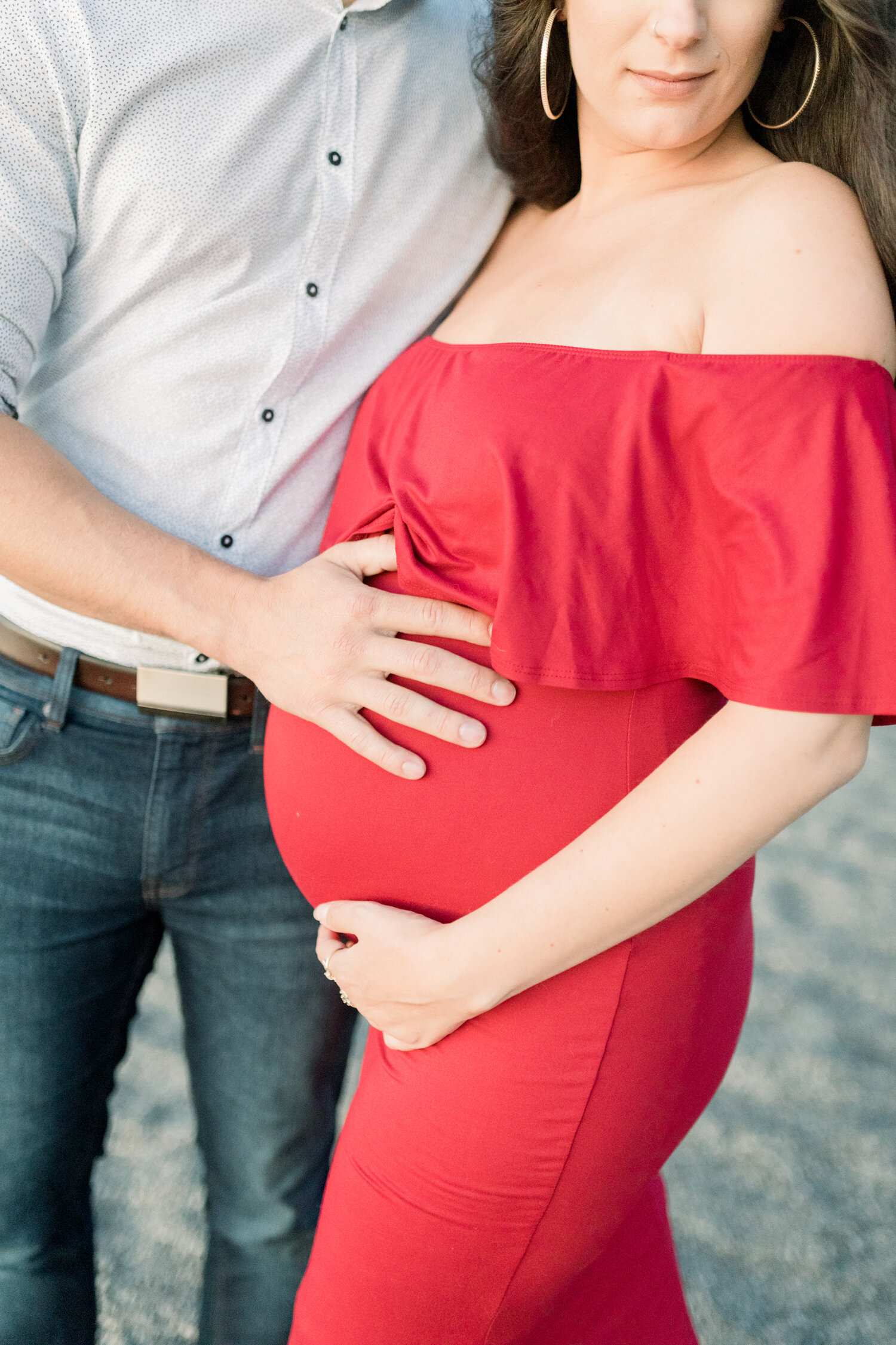  During this Ottawa, Canada maternity shoot, Chelsea Mason Photography captures this up-close detailed shot of this expectant couple cupping a baby belly. maternity photos ottawa canada, fitted red off the shoulder maternity dress, beach maternity ph