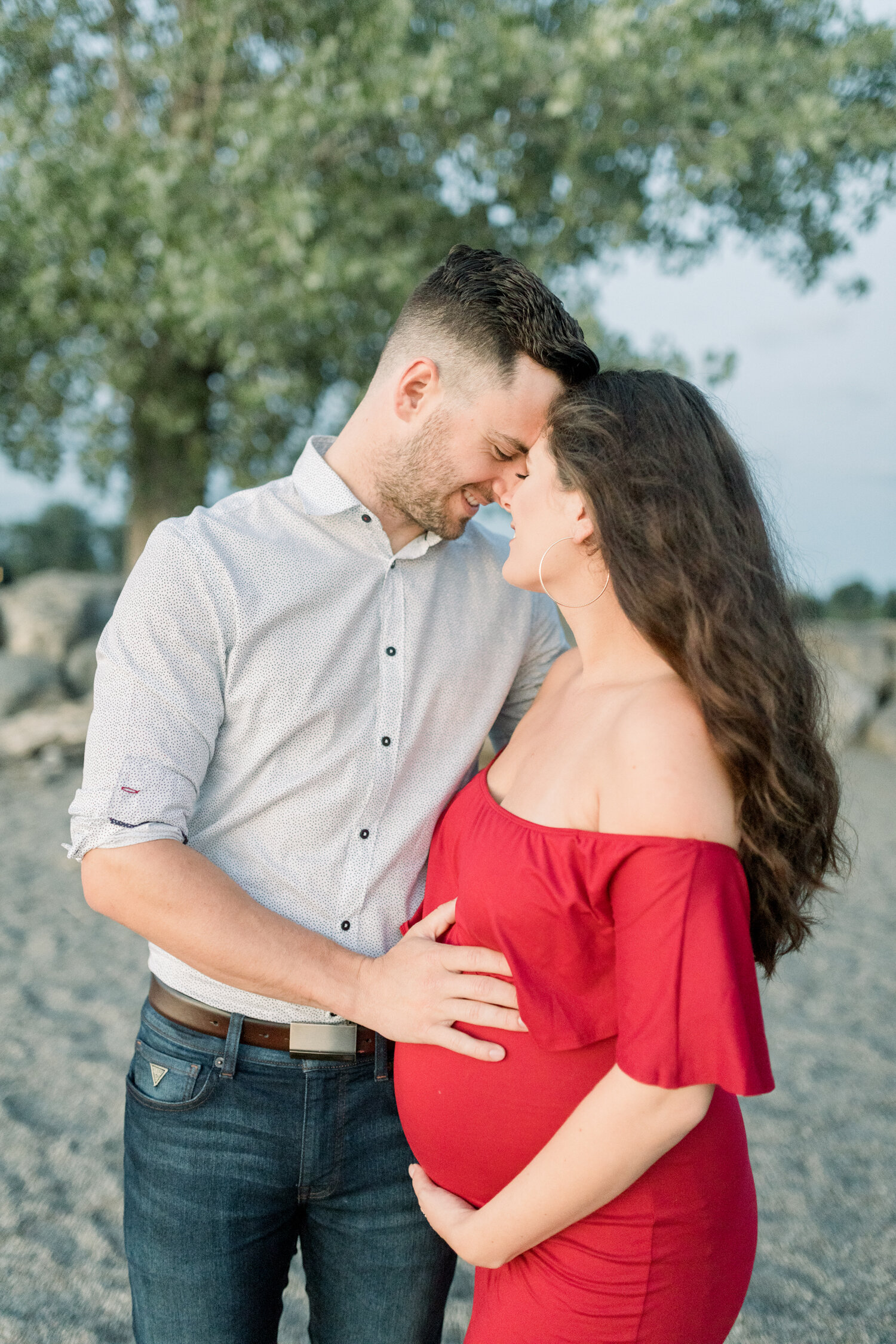  During this romantic maternity session along Brittania Beach in Ottawa, Canada, Chelsea Mason Photography captures this couple lovingly press their foreheads together while holding a baby bump. baby bump, husband holding pregnant belly, fitted off t