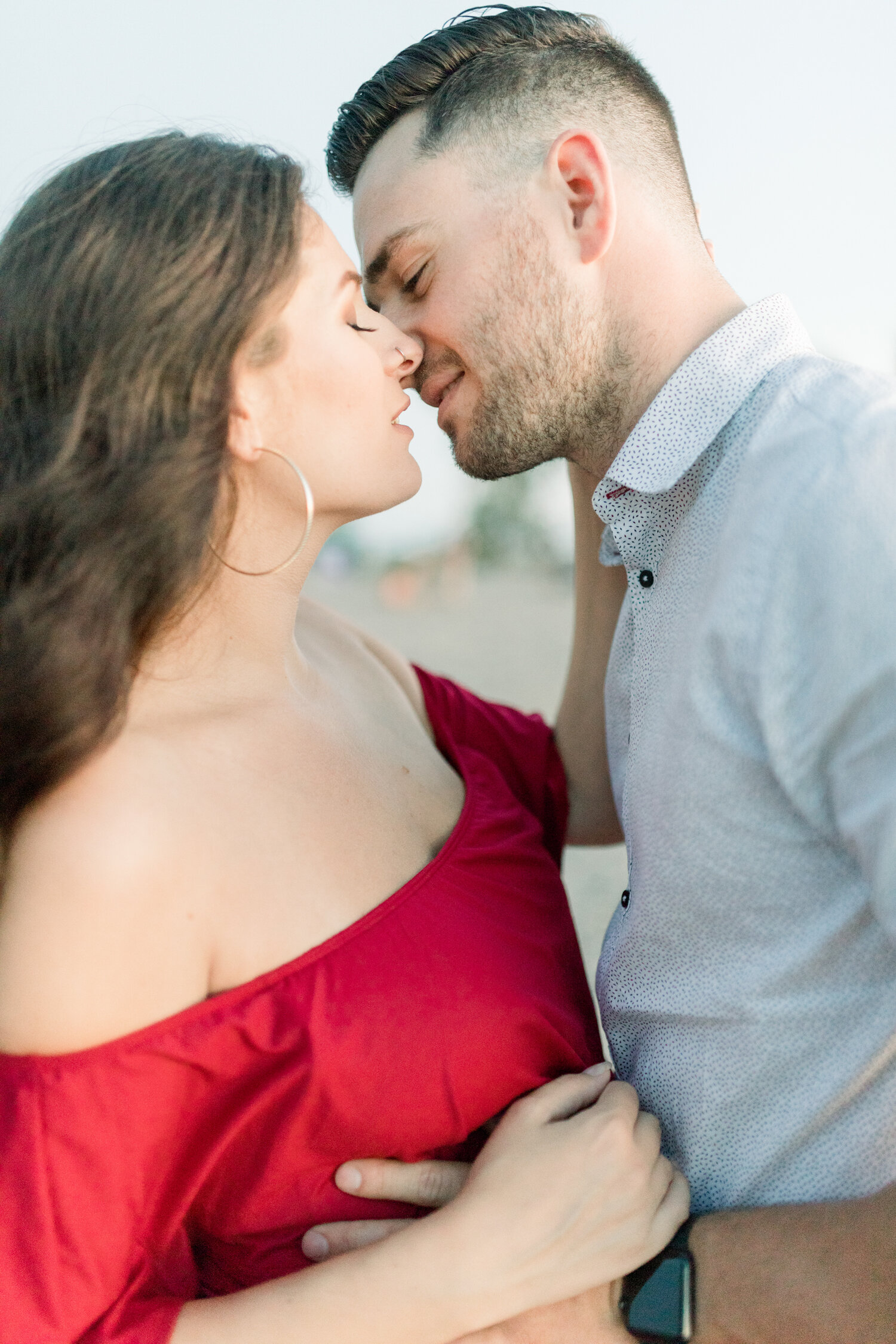  During this sunset beach maternity session in Ottawa, Canada, Chelsea Mason Photography captures this expectant couple share a romantic kiss. romantic couple kissing, sunset beach maternity session, fitted red maternity dress, off the shoulder women