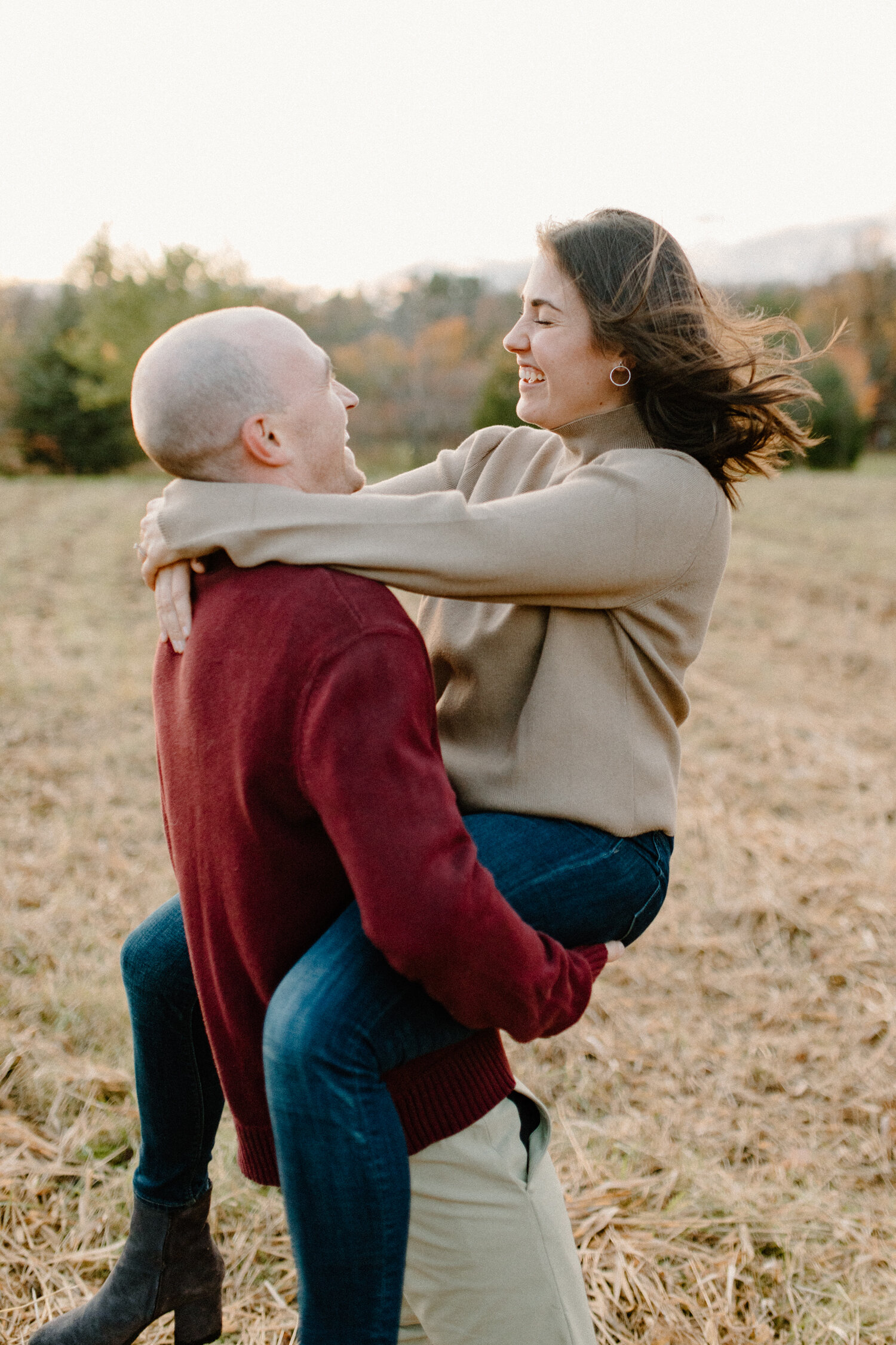  While posing for their engagement session in Ontario, Canada, this soon-to-be bride wraps her arms and legs around her fiance and laughs playfully for photos with Chelsea Mason Photography. red camel and denim colored engagement outfit ottawa canada
