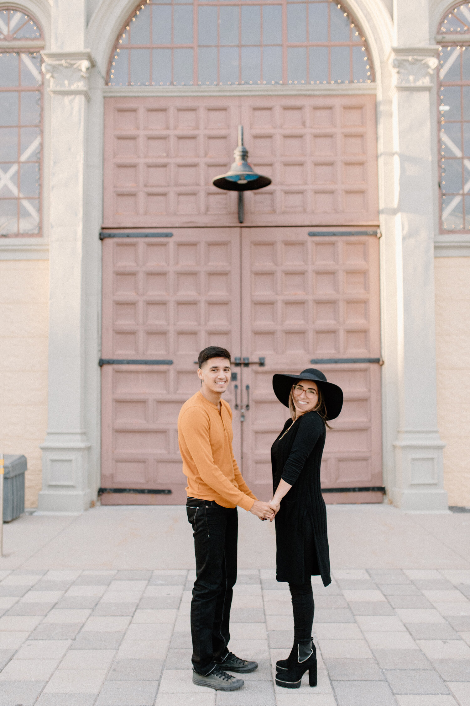  During this engagement session outside the Ottawa Horticulture Building, Chelsea Mason Photography captures this couple holding hands. black and orange engagement outfit colors urban engagement photos ontario canada womens black hat ontario canada e