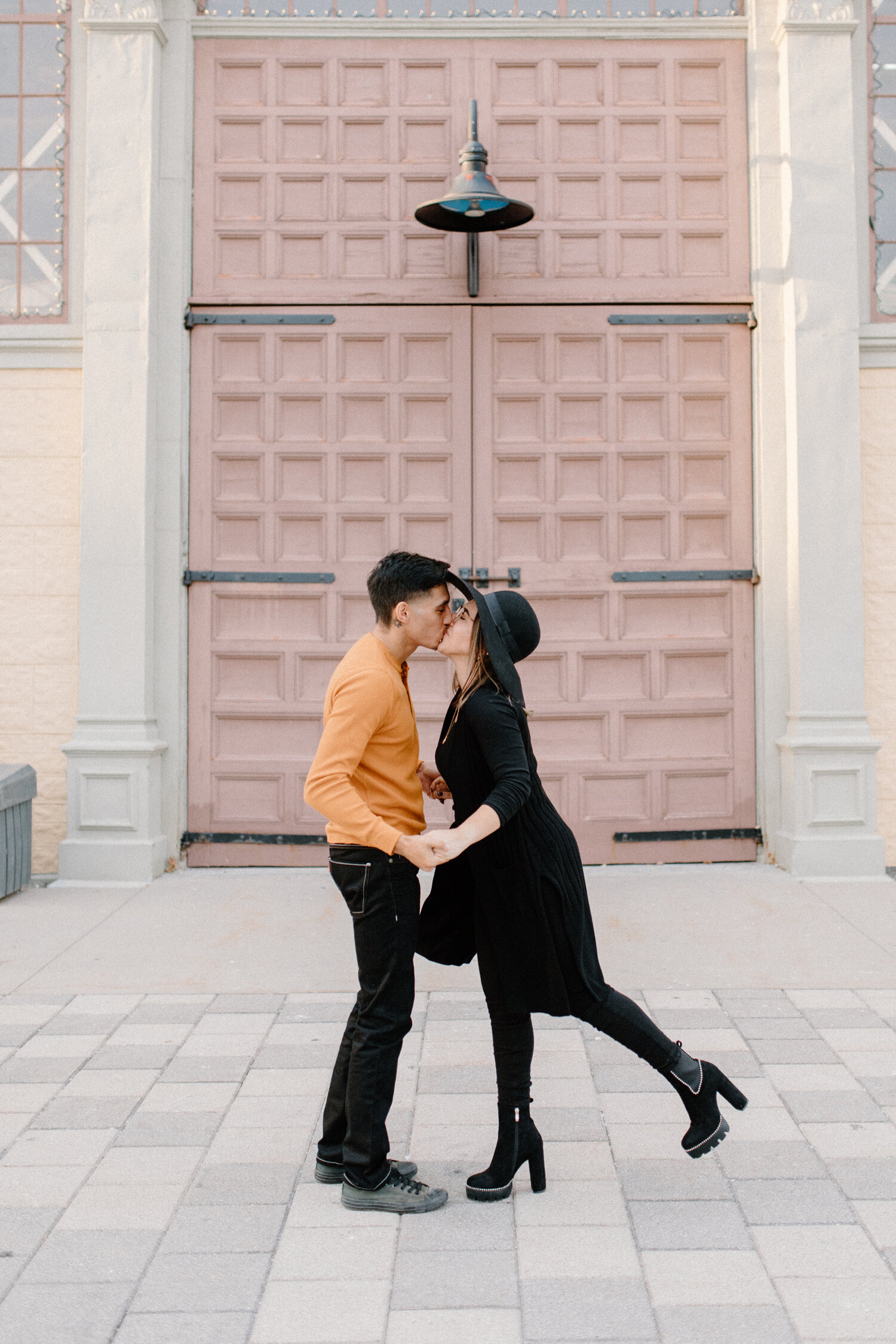  During this urban engagement session in Ontario, Canada, Chelsea Mason Photography captures this couple holding hands and leaning in for a kiss outside the Horticulture Building. womens all black engagement outfit mens black denim pants gray mens va