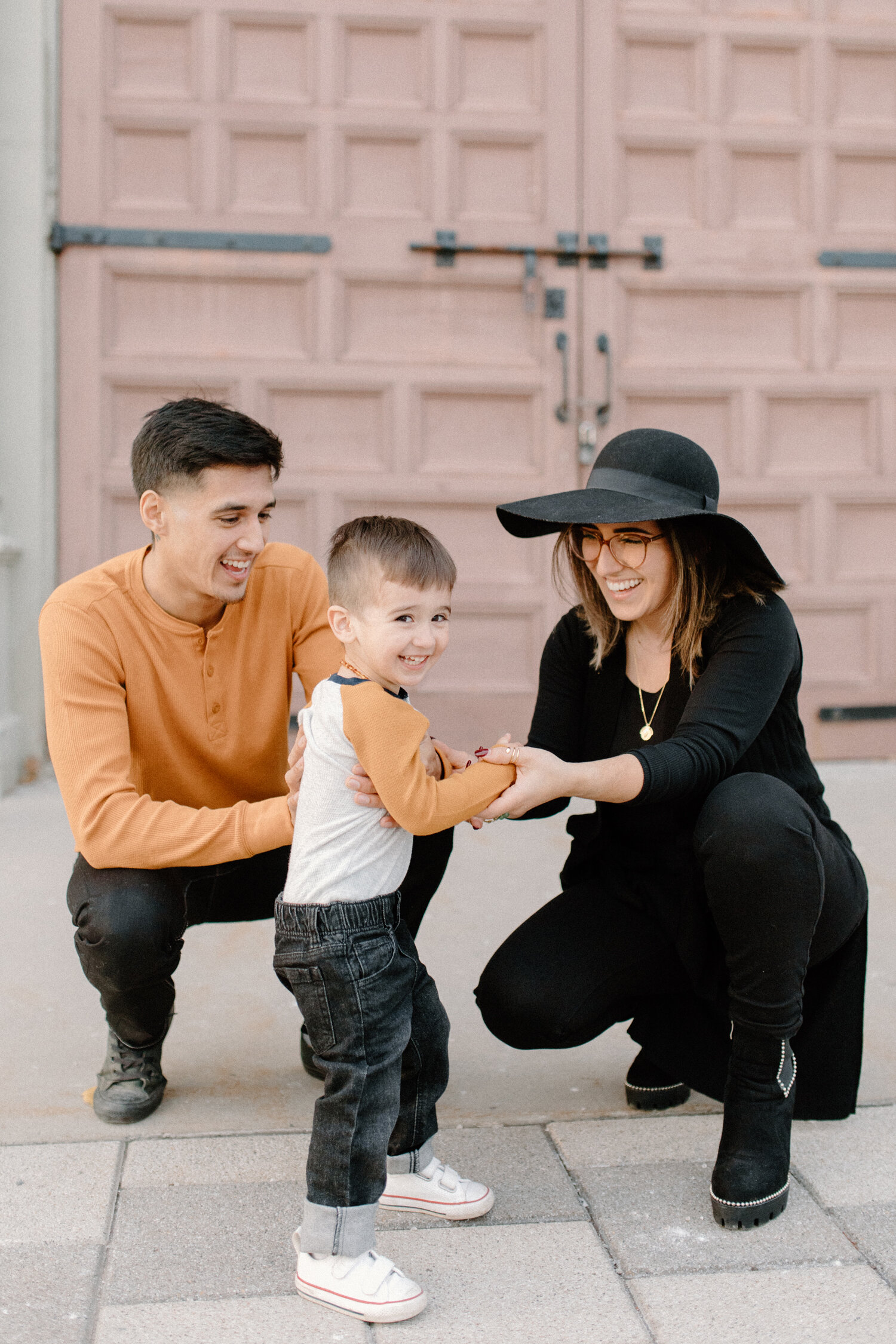  Ottawa, Canada’s Chelsea Mason Photography captures this family of three kneeling down and holding hands outside the Horticulture Building. urban engagement session location ottawa canada orange and black family photo outfit colors laughing family w