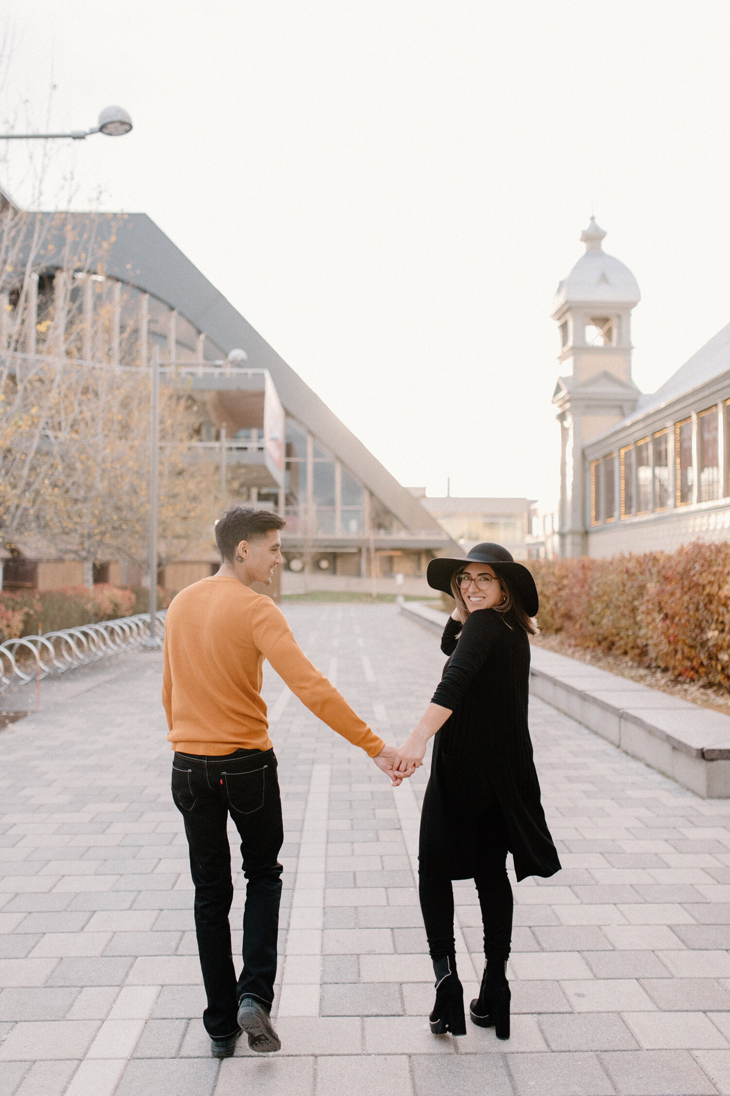  During their urban engagement session, Chelsea Mason photography captures this couple holding hands and smiling outside the Ottawa, Canada Horticulture Building. urban engagement session orange and black engagement outfit colors couple holding hands