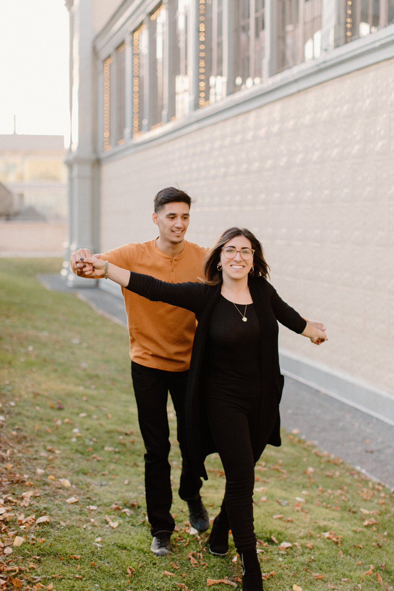 Ontario, Canada photographer, Chelsea Mason Photography captures this couple holding one another’s hands while playfully walking alongside the Horticulture Building. urban engagement session, orange and black colored engagement session outfit colors