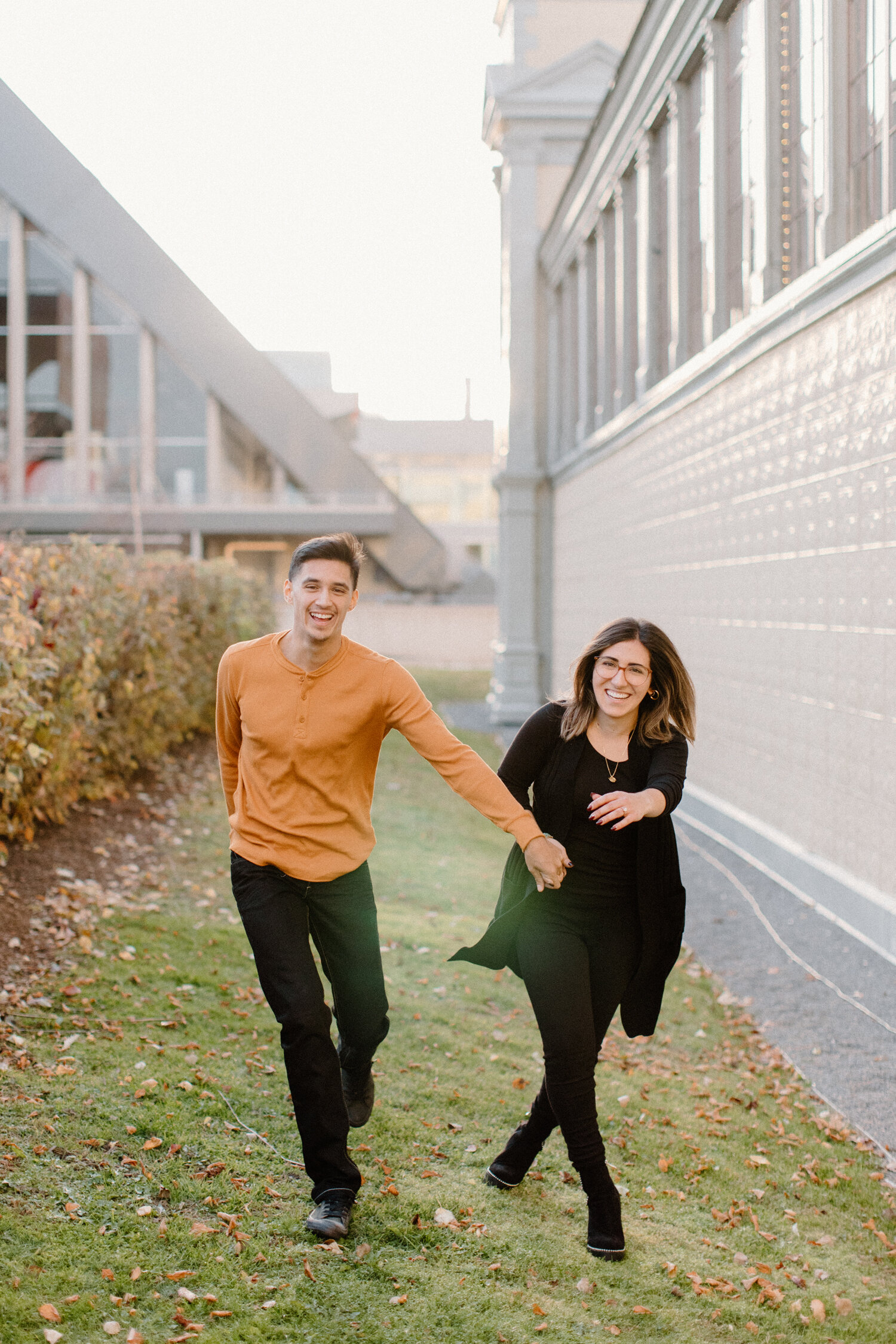  While running beside the Ottawa, Ontario Horticulture Building, Chelsea Mason Photography captures this couple running and holding hands playfully. orange and black family photo outfit colors couple playfully holding hands womens thick rimmed oversi