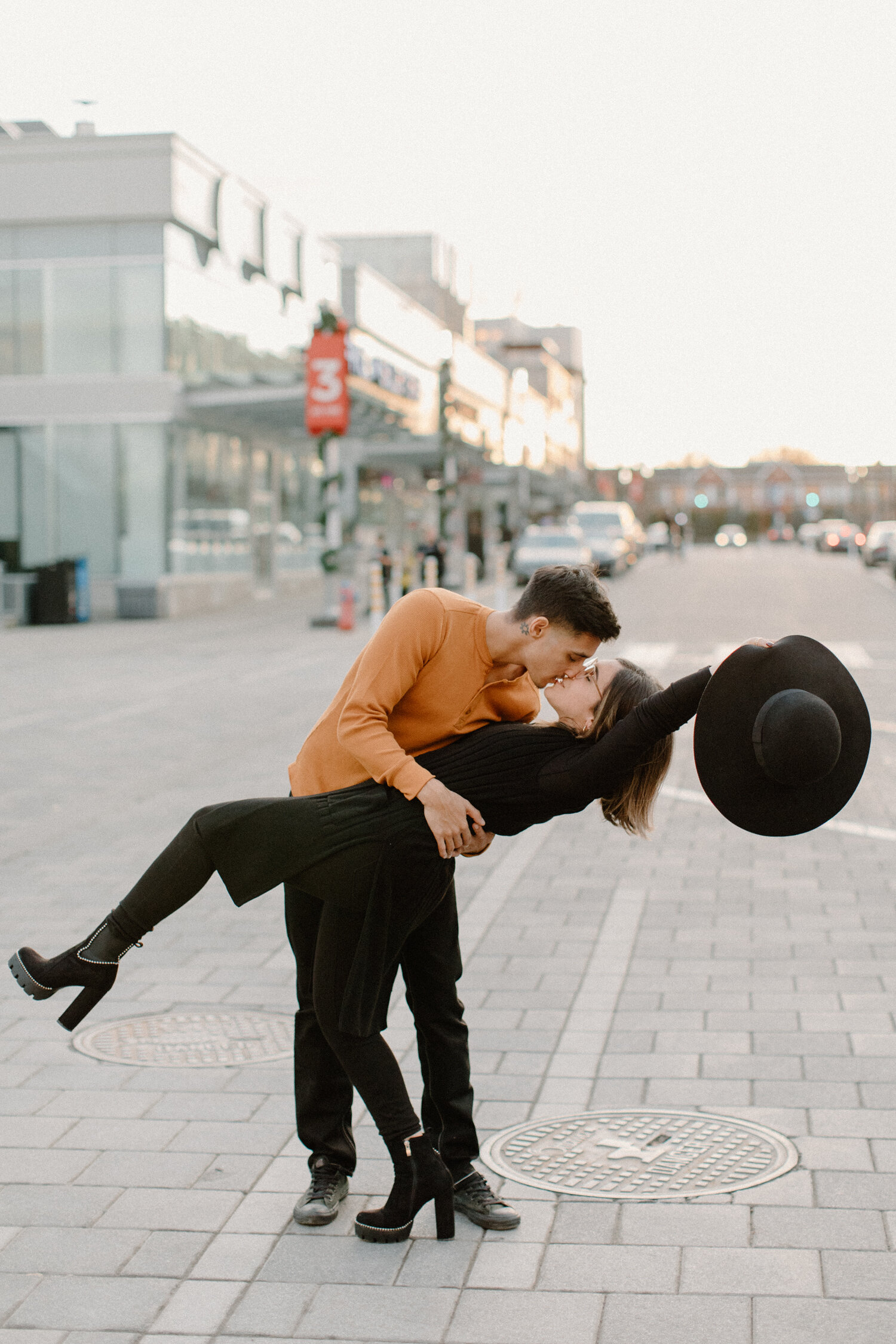  With an urban setting in the backdrop and cars wizzing by, Ontario, Canada couples photographer, Chelsea Mason Photography captures this soon-to-be groom dipping his fiance for a kiss. dipping and kissing, woman raising brimmed hat in air while kiss