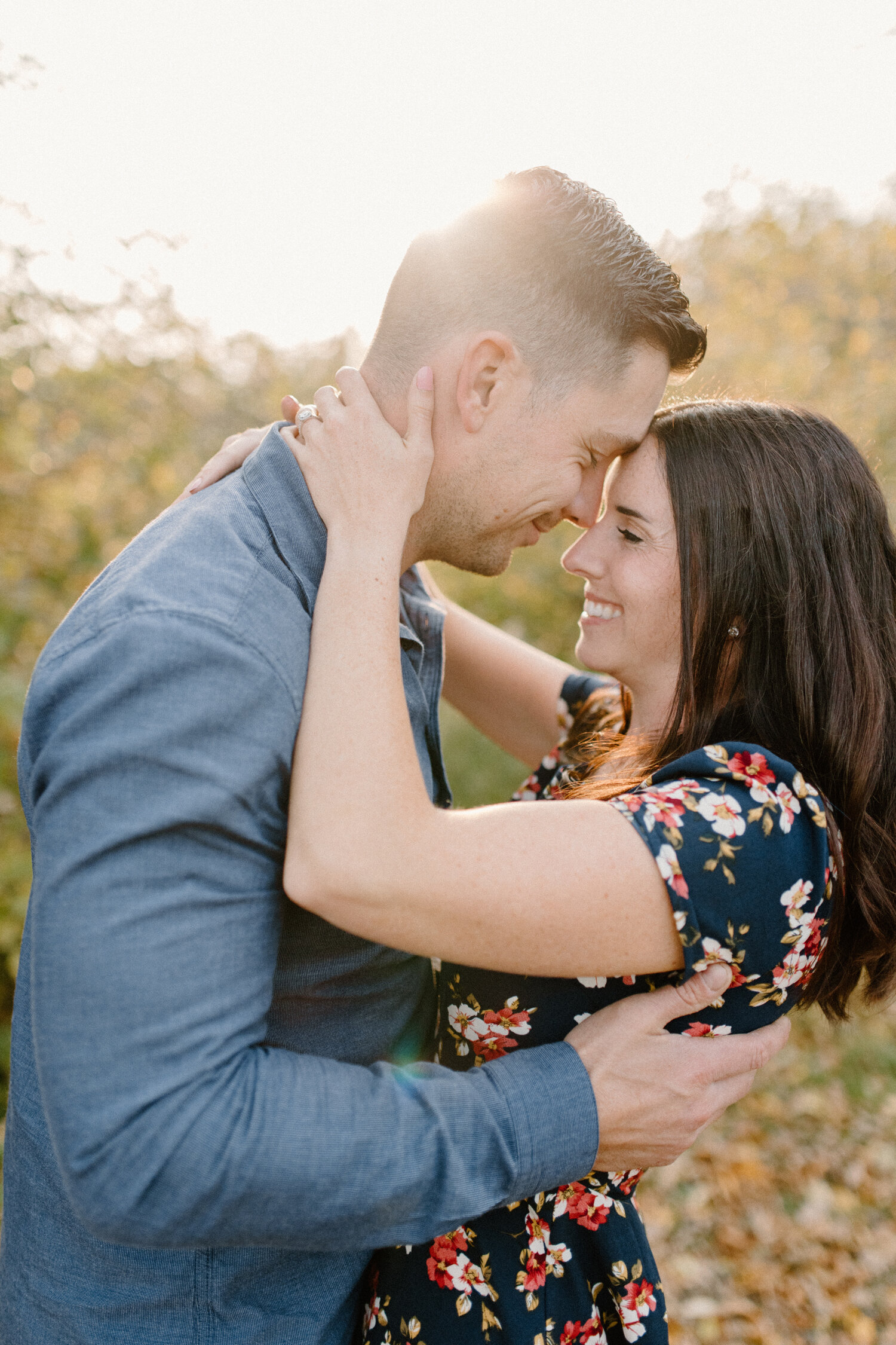  Chelsea Mason Photography captures this couple pressing their foreheads together and smiling during their engagement session in the autumn leaves of Brockville, Ontario. mens medium blue button up shirt couple pressing foreheads together smiling wom