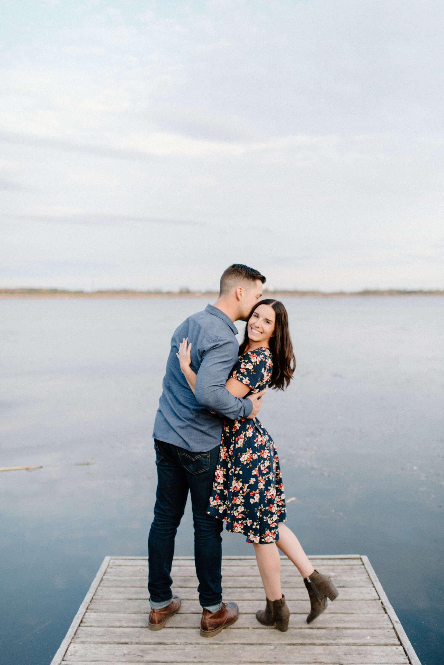  On the pier of a lake in Brockville, Ontario, Chelsea Mason Photography captures this couple hugging romantically overlooking the sunset. sunset pier engagement session brockville ontario womens high low navy floral womens dress with heeled booties 
