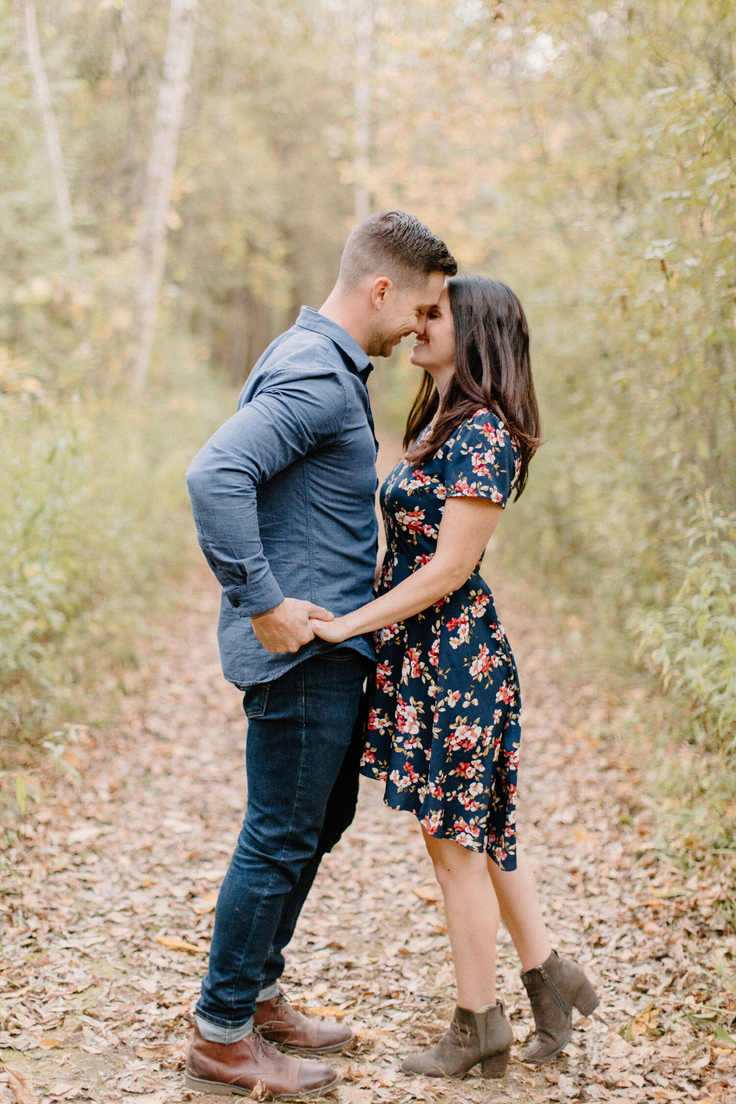  Stopped on an unpaved dirth pathway with falled autumn leaves, Brockville, Ontario photographer, Chelsea Mason Photography captures this couple holding hands and leaning in for a romantic kiss. womens high low floral dress with cap sleeves mens all 