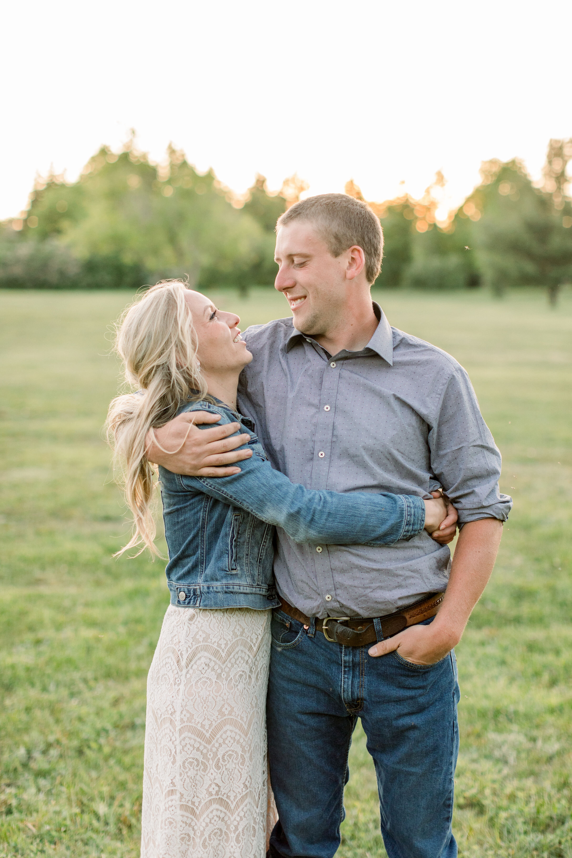  Posed in a grassy field in Ontario, Canada, Chelsea Mason Photography captures this engaged couple wrapping their arms around one another and smiling. man wrapping arms around fiancé and smiling down at her engagement outfit inspiration #ChelseaMaso