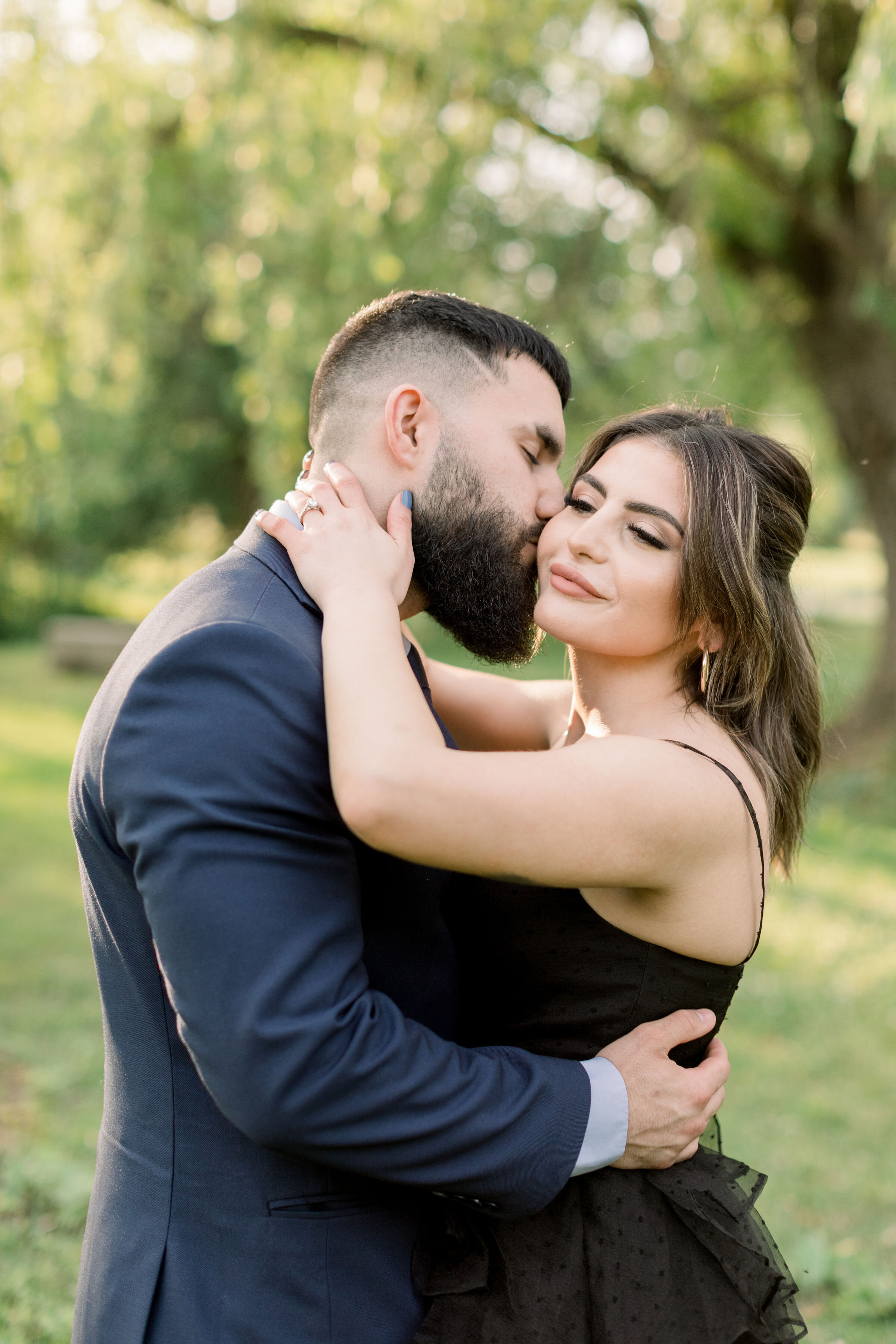  During this formal engagement shoot in Ottawa, Ontario, Chelsea Mason Photography captures this groom kiss his fiance's cheek romantically. women's formal black spaghetti strapped tea dress man kissing woman's cheek Ottawa Canada engagement photogra