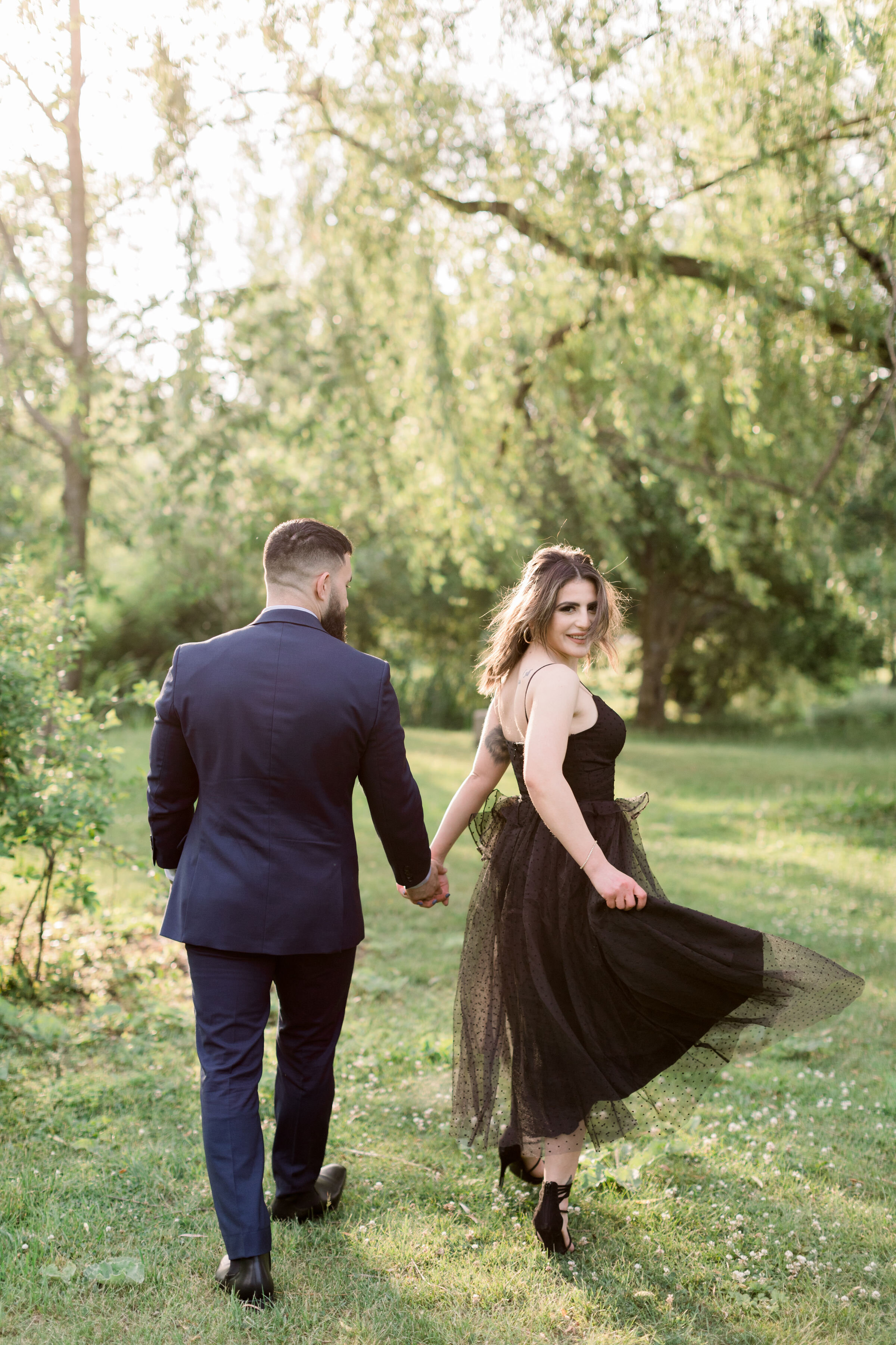  While walking through a shaded grassy park, Ottawa, Ontario photographer, Chelsea Mason Photography captures this formally dressed engaged couple holding hands and looking over their shoulder. formal engagement photo outfits women black tea length d