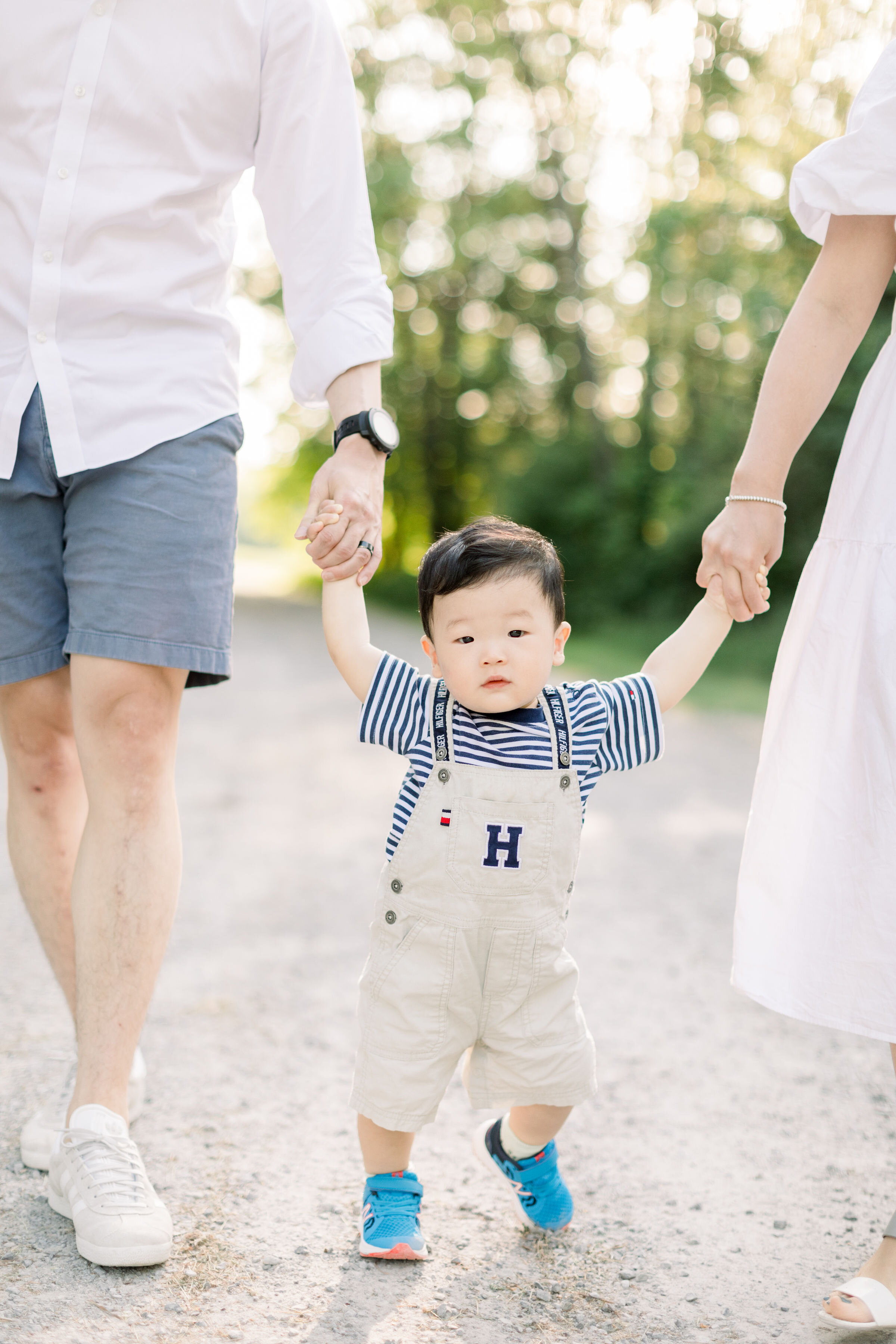  While holding his parents hands as they walk down a gravel pathway, Ottawa family photographer, Chelsea Mason photography captures a candid up-close photo of this toddler boy. toddler candid portrait summer family photos Ottawa Canada #ChelseaMasonP