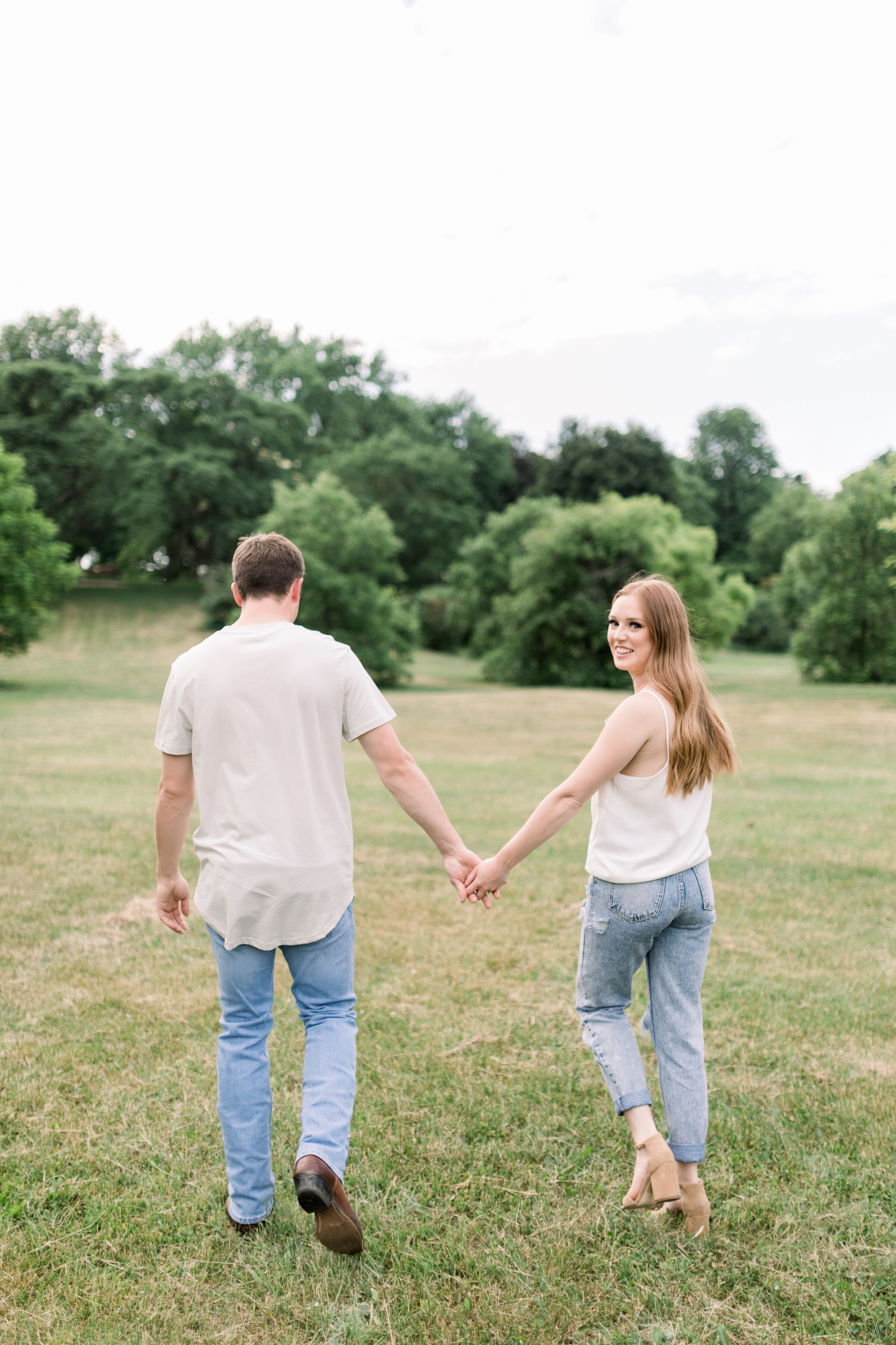  Ottawa, Ontario couples photographer, Chelsea Mason Photography captures this engaged couple walking hand-in-hand through a grassy field. grassy field engagement session Ottawa Ontario couples photographer neutral engagement photo outfits #ChelseaMa