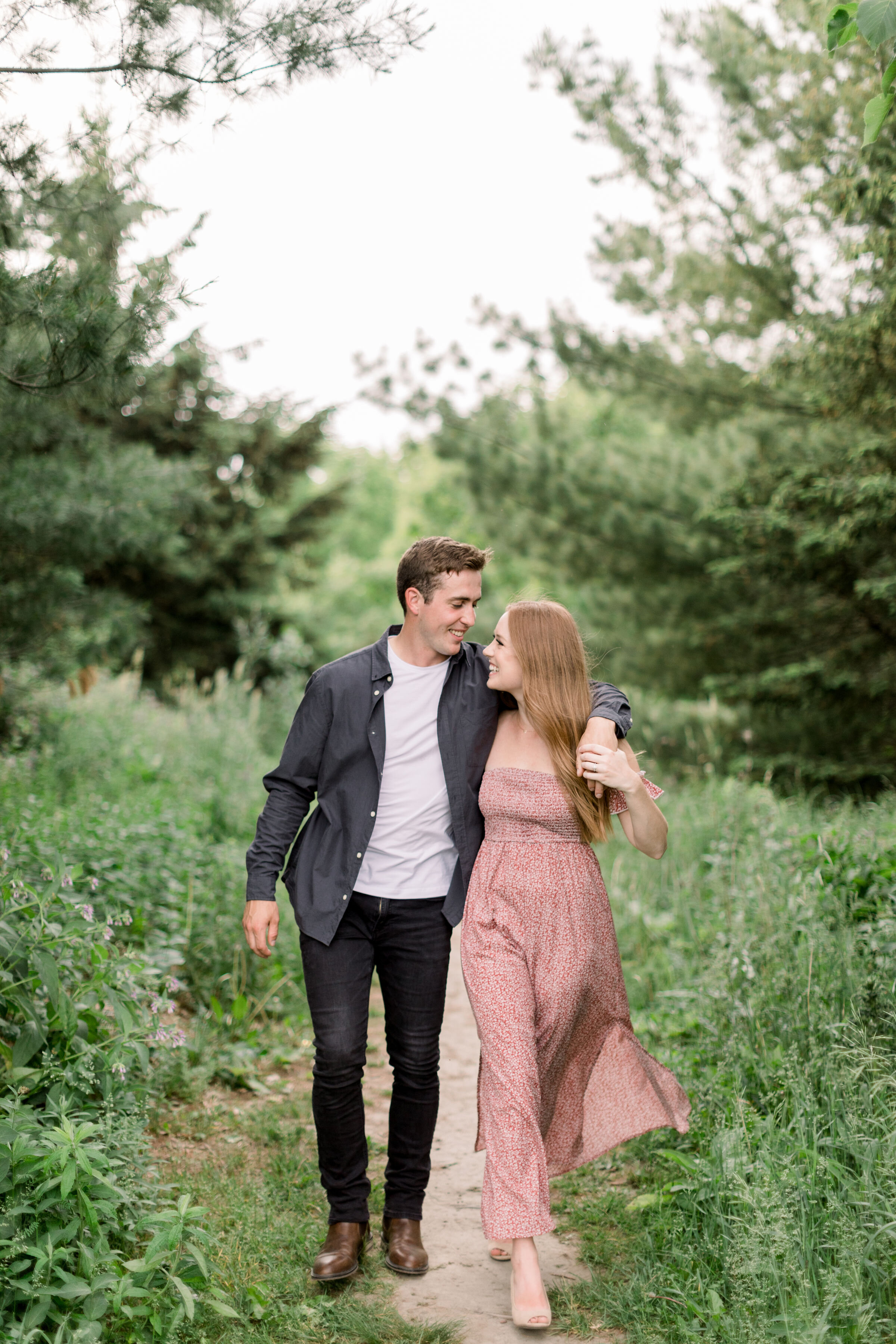  Arboretum, Ottawa's Chelsea Mason Photography captures this soon-to-be groom wrap his arms around his fiancé while they walk through an unpaved pathway during their engagement session. engaged couple poses authentic couple poses playful engagements 