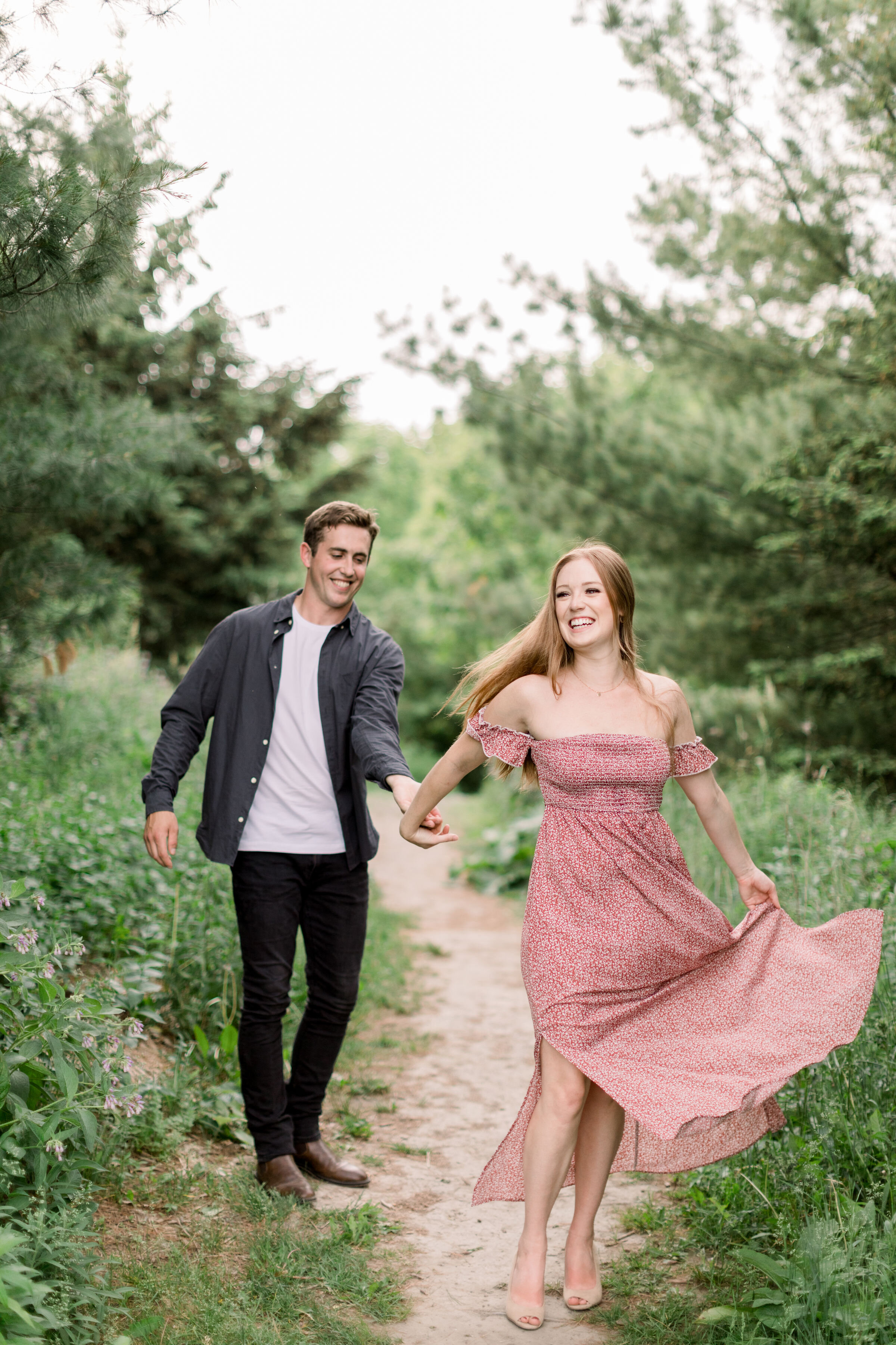  In Arboretum, Ottawa, Chelsea Mason Photography captures this soon-to-be bride playfully leading her fiancé through an unpaved shaded pathway during their engagement shoot. playful running engagement poses formal engagement outfits women's off the s