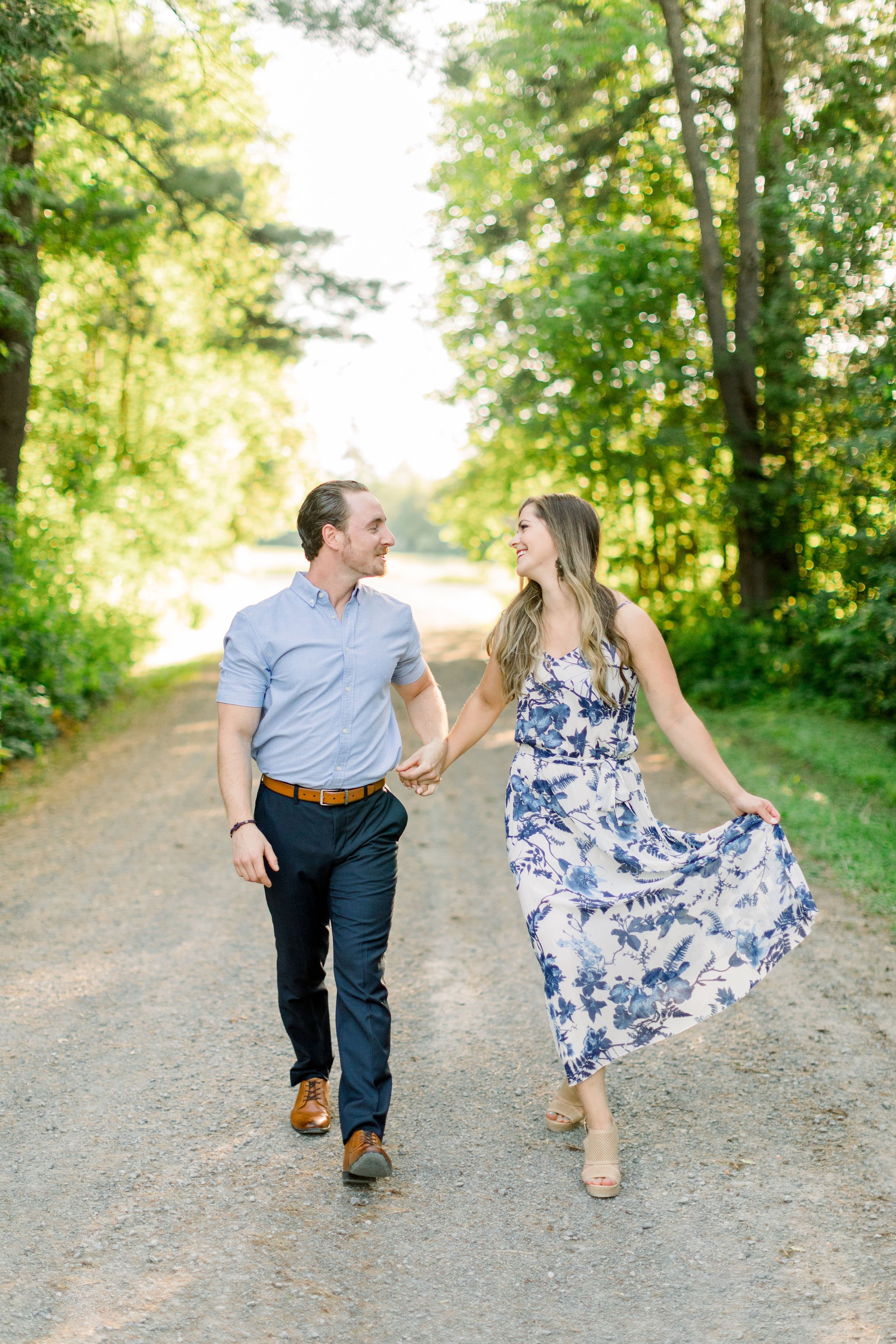  Walking on a dirt road a newly engaged couple holds hands captured by Chelsea Mason Photography. dirt path blue dress #chelseamasonphotography #chelseamasonengagements #millofkintail #Ottawaengagments #Almonteengagementphotographer #outdoorengagment
